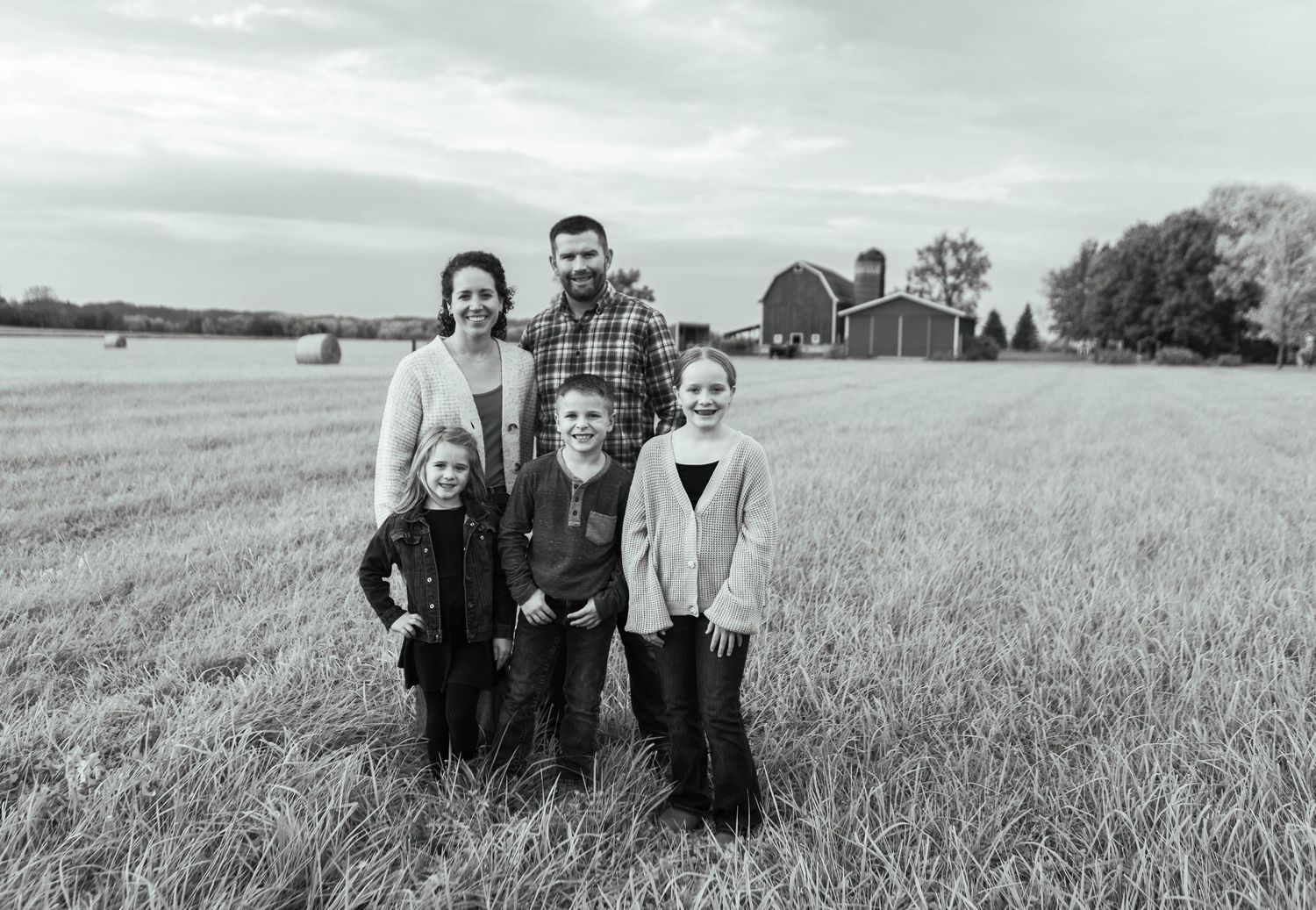 Black and white portrait of family group in rural field with barn. Mauston photographer.