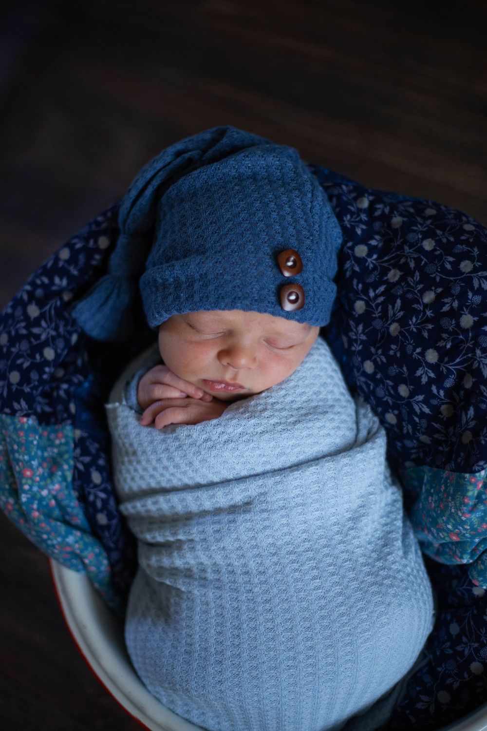 Newborn wrapped in white knit blanket wearing navy blue cap and floral outfit. Mauston photographer.