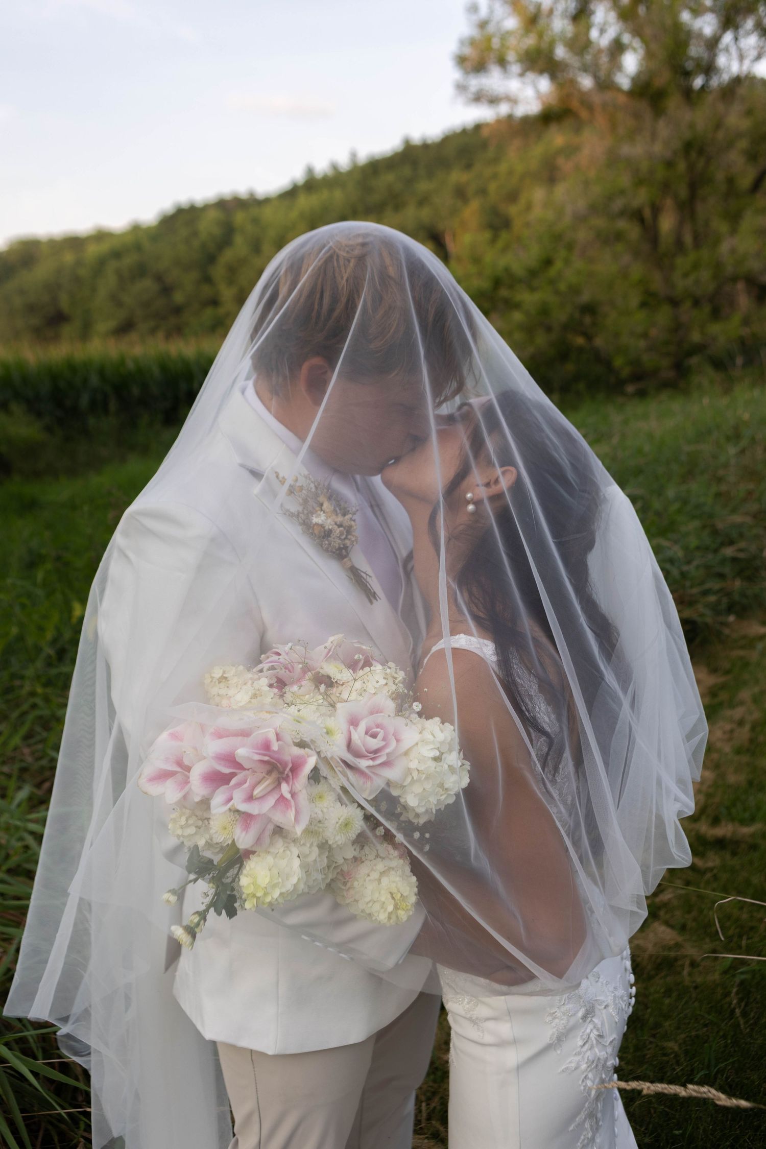 Romantic wedding photo of couple sharing intimate moment under flowing veil outdoors. Mauston photographer.
