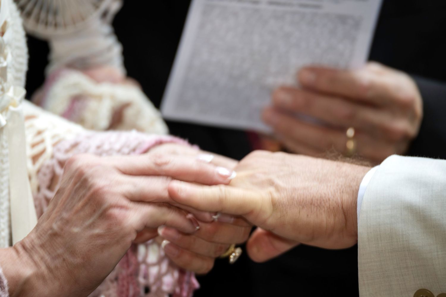 Elderly couple exchanging wedding rings during a marriage ceremony, with an officiant holding a document in the background.