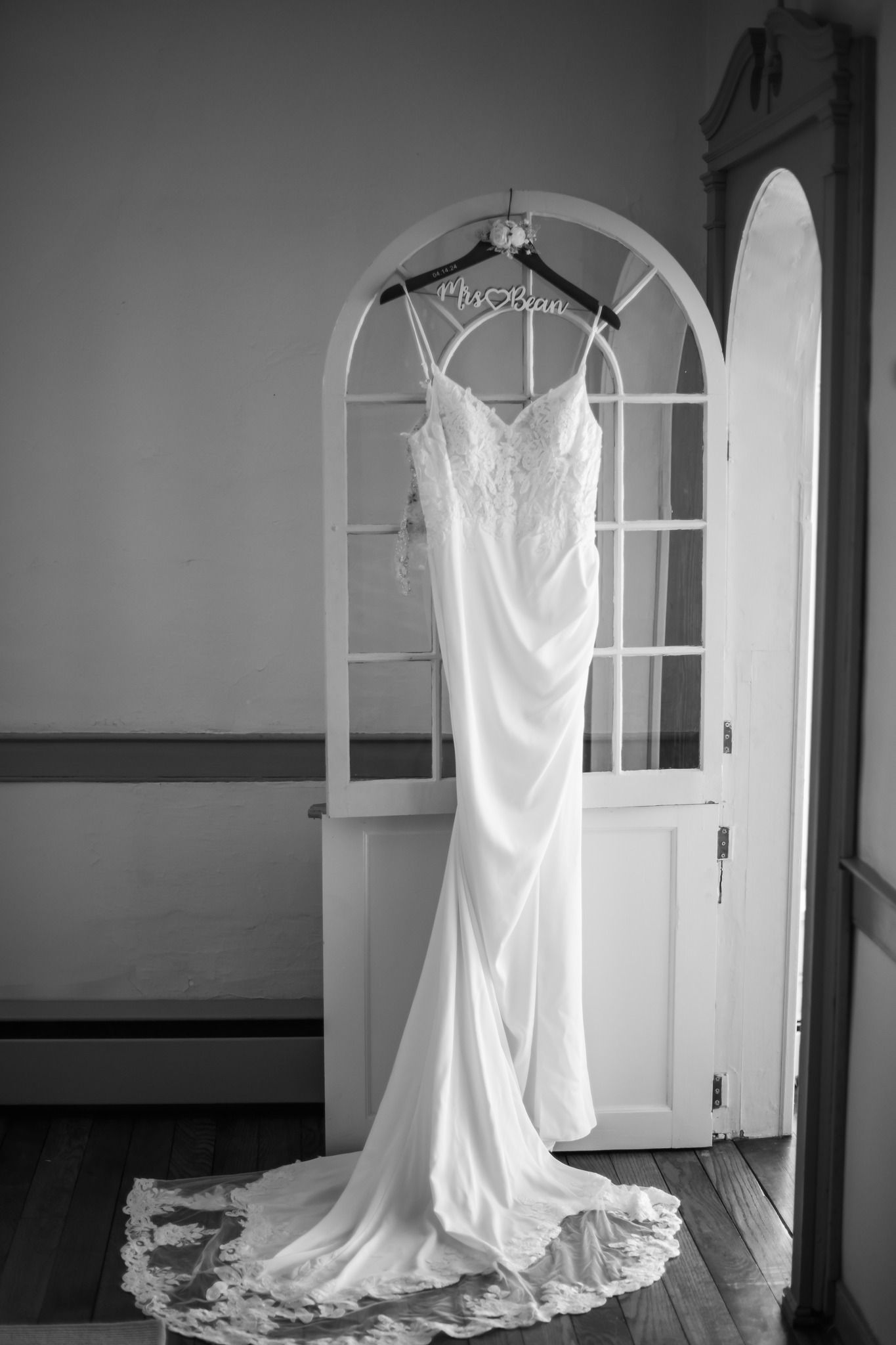 Black and white image of elegant wedding dress hanging on personalized bridal hanger.