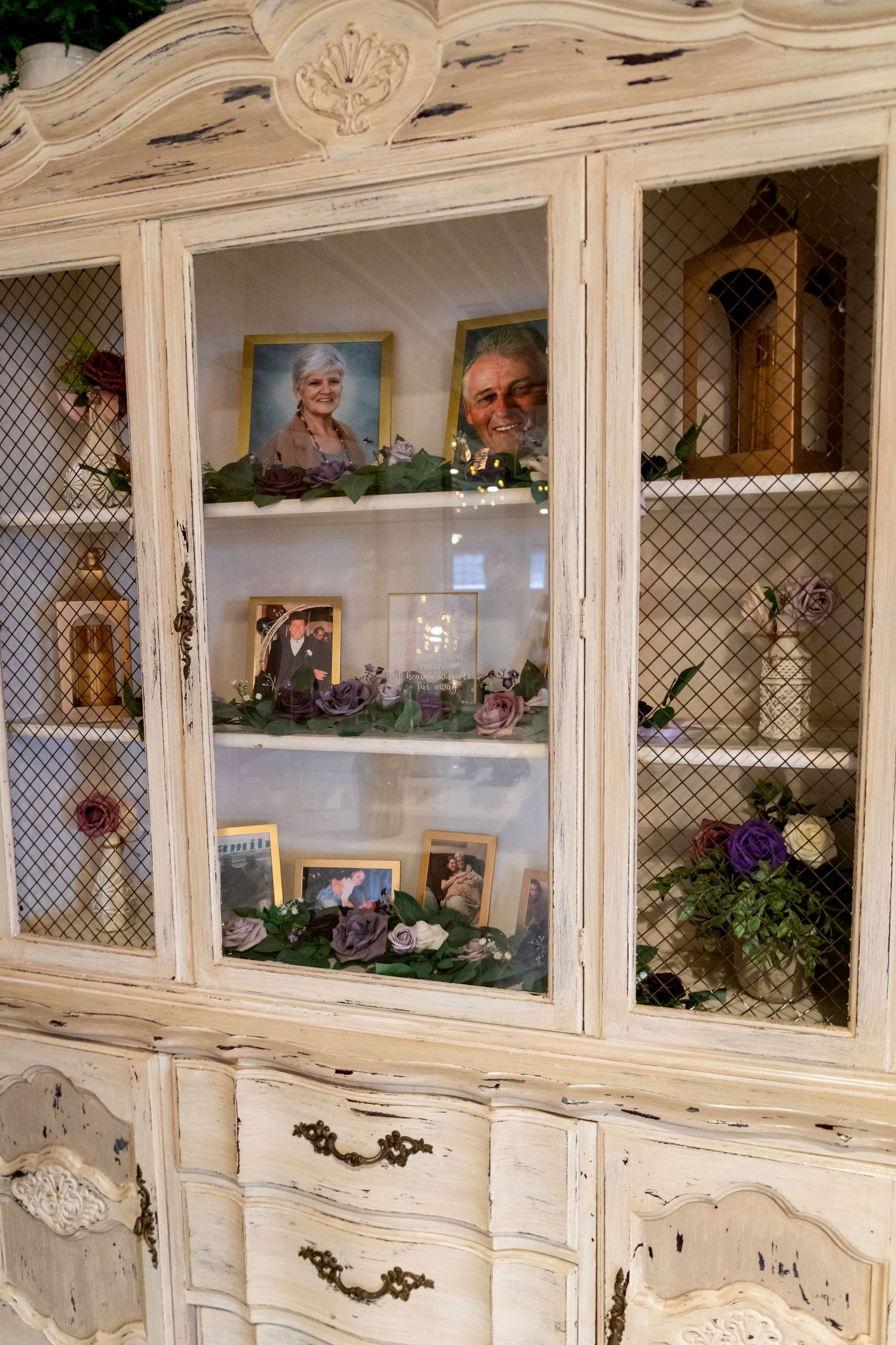 Vintage cream-painted china cabinet displaying framed family photos and decorative items at a wedding reception.