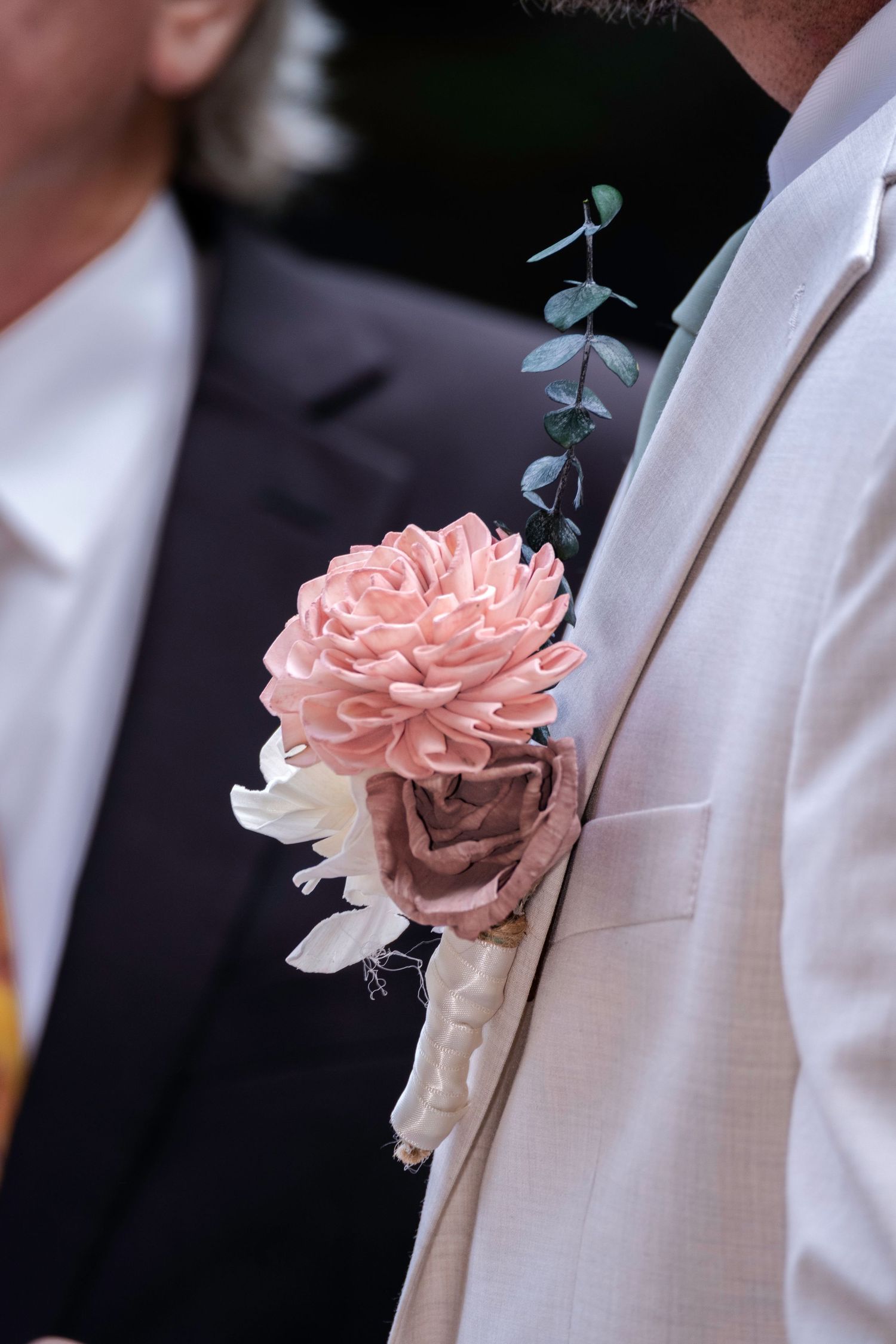 Close-up of a groom's boutonniere featuring pink and mauve roses with eucalyptus on a cream suit lapel.