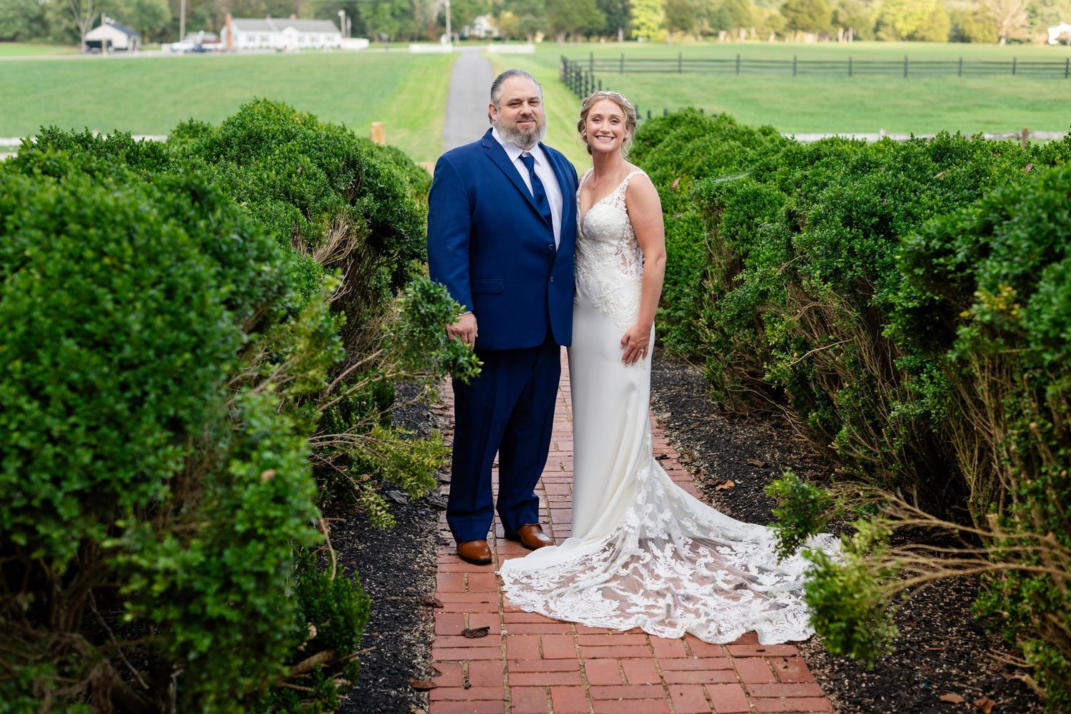 Bride and groom posing on a brick path surrounded by lush green hedges at an outdoor wedding venue.
