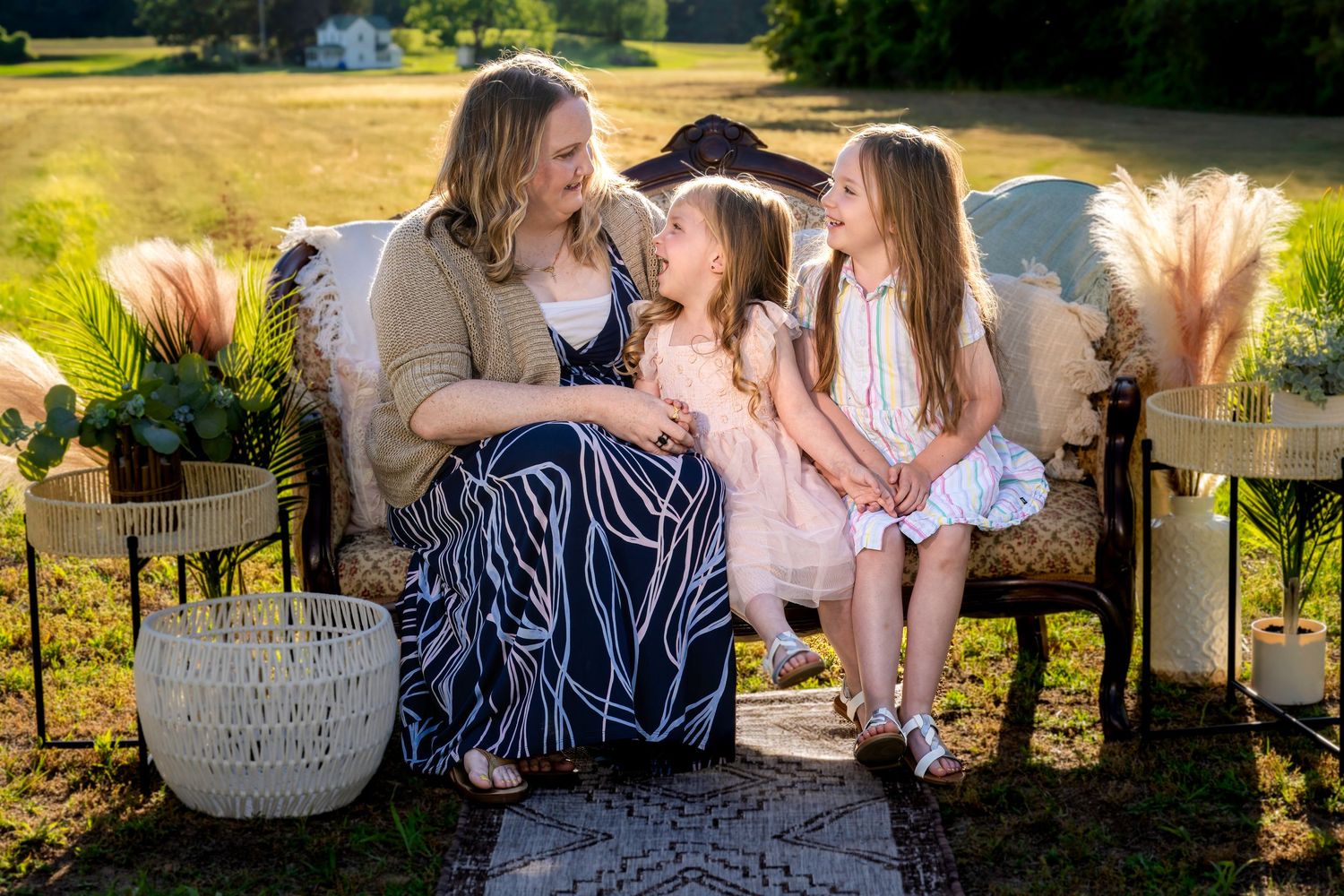 A mother and two young daughters share a joyful moment on a vintage sofa outdoors in golden hour light.