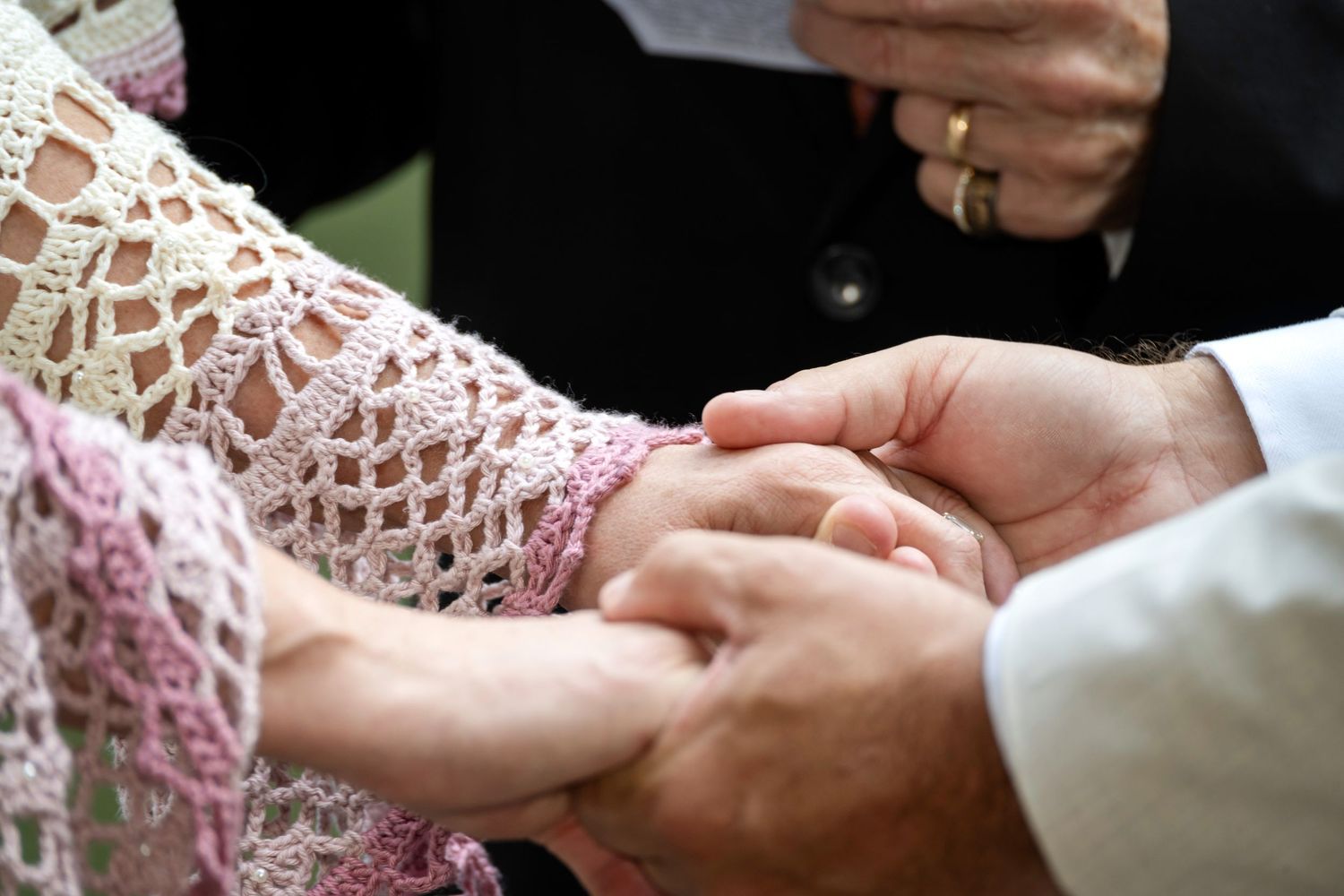 Close-up of a couple holding hands during a wedding ceremony, bride wearing a pink crochet dress.