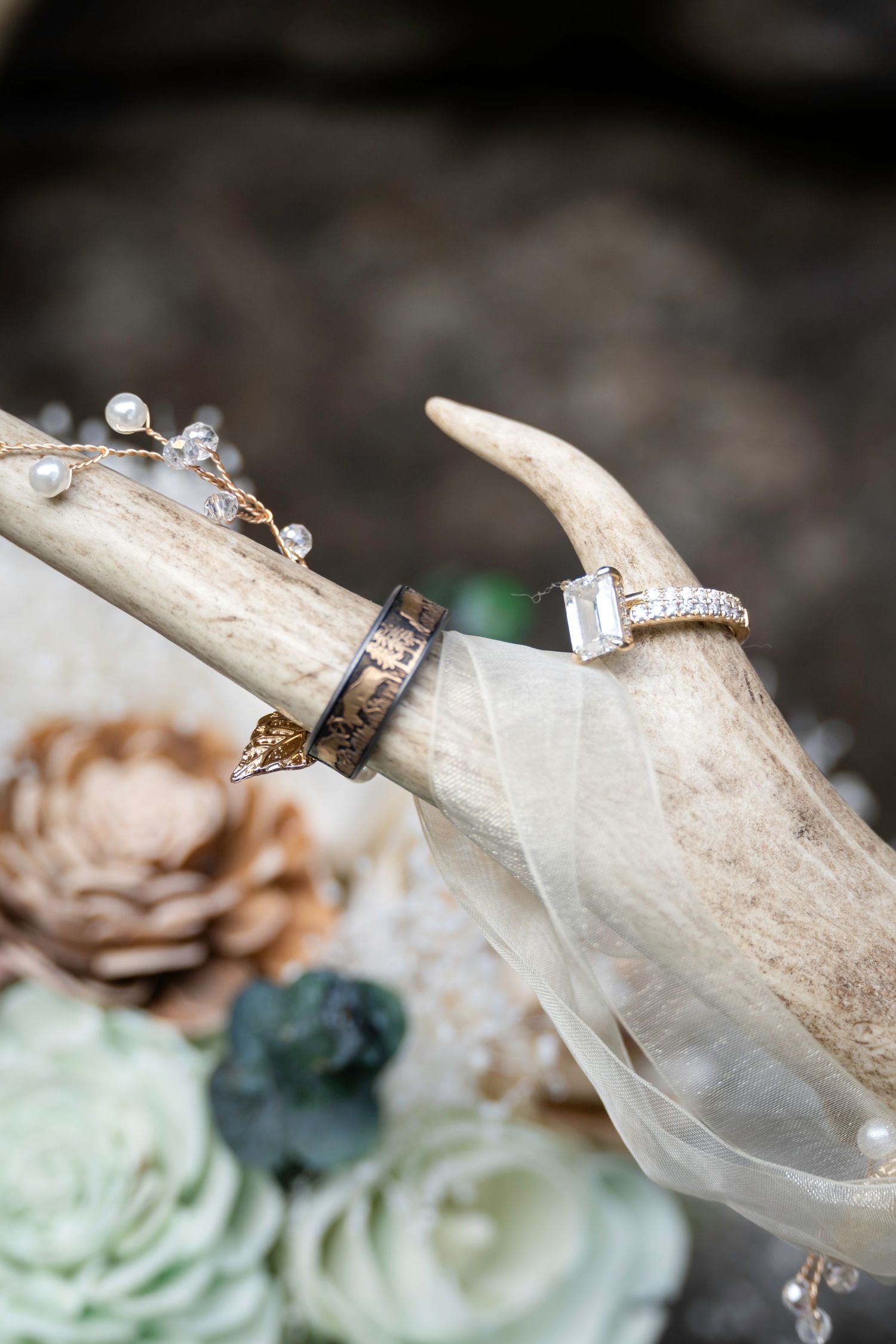 Two wedding rings displayed on a rustic deer antler with flowers and greenery in a bohemian wedding flat lay.