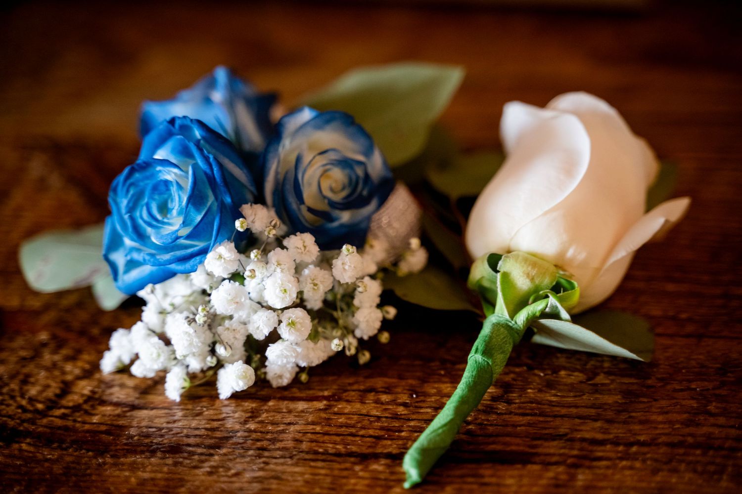 Blue and white rose boutonnieres with baby's breath on rustic wooden surface.