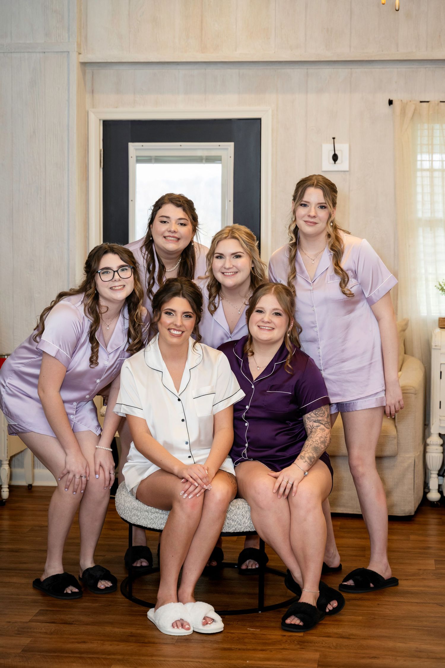 Bride and bridesmaids in purple and white pajama sets smiling together in bridal suite getting ready.