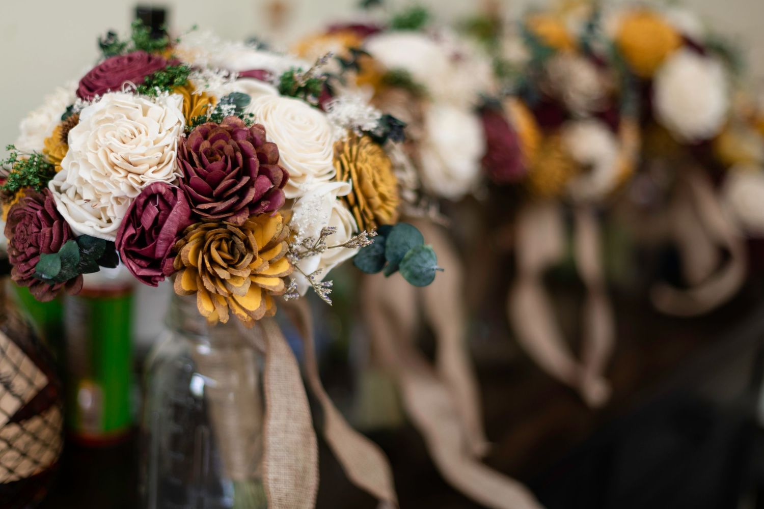 Rustic wedding bouquets with burgundy, mustard, and cream sola wood flowers in mason jars with burlap ribbons.