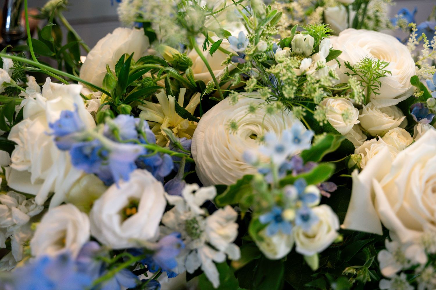 Close-up of elegant white and blue floral arrangement featuring ranunculus, lisianthus, and delicate blooms.