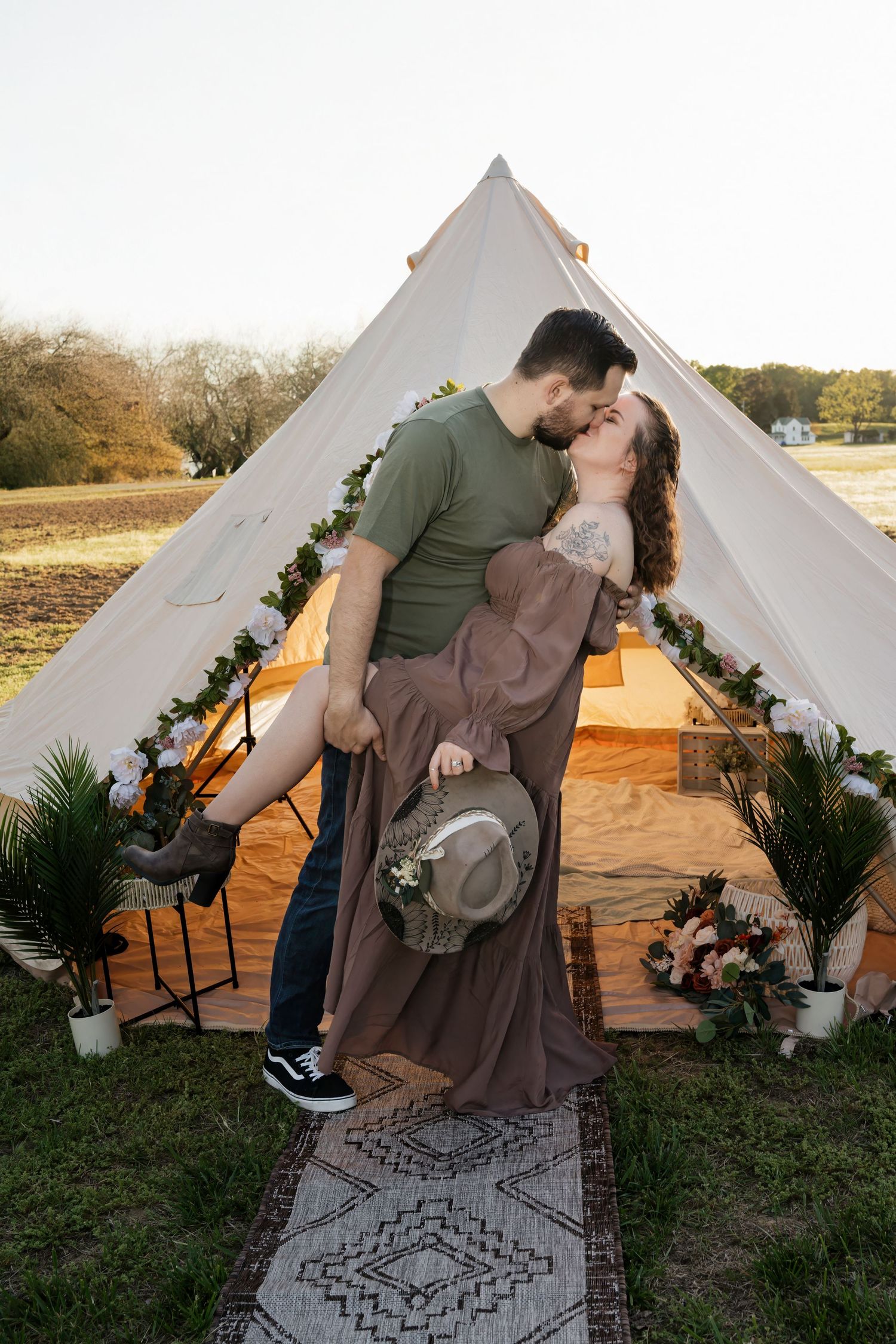Couple sharing a romantic dip kiss in front of a decorated bell tent with floral garlands at a boho outdoor setting.