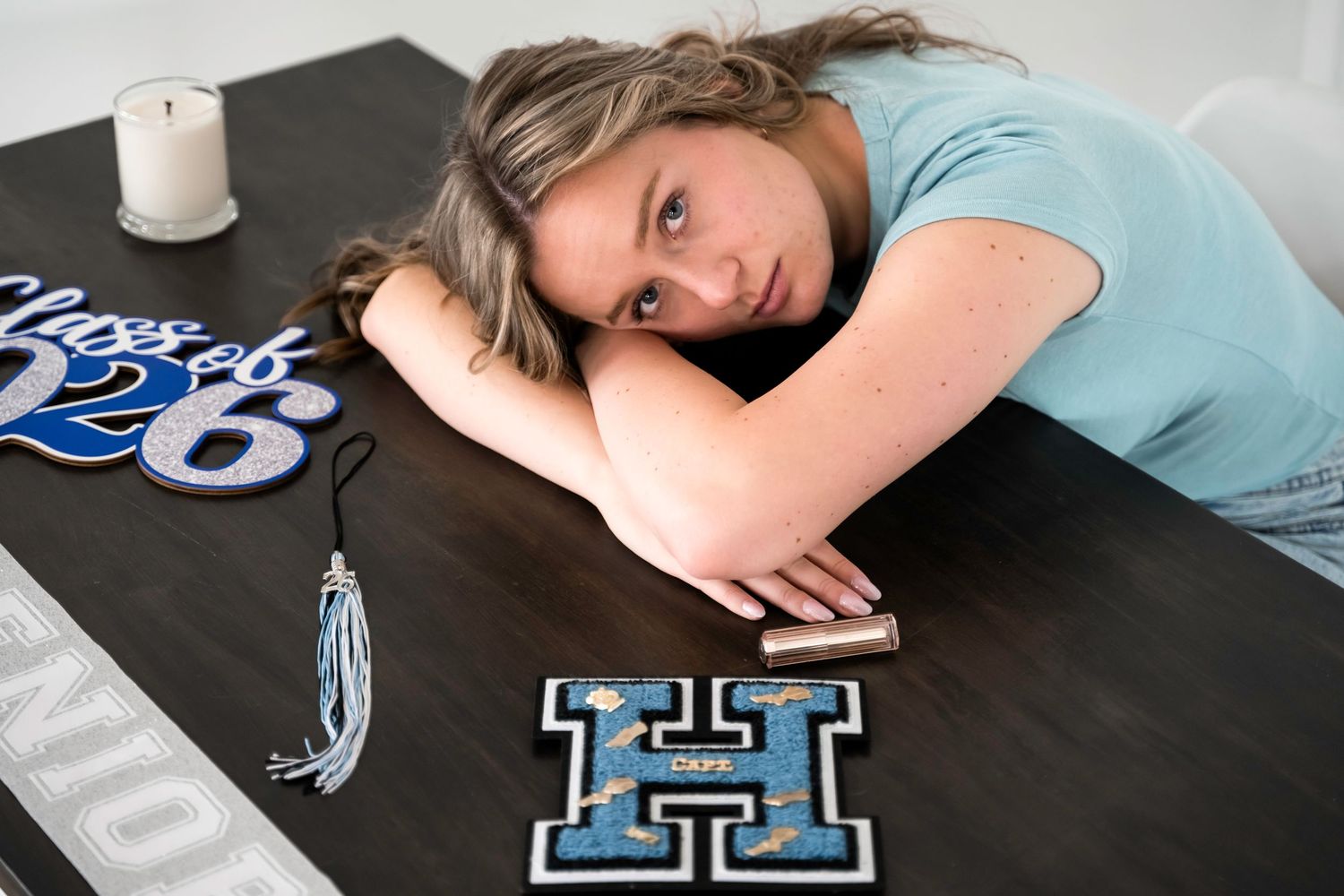 Teen girl posing with Class of 2026 graduation decorations, varsity letter H, and tassel on a dark table.