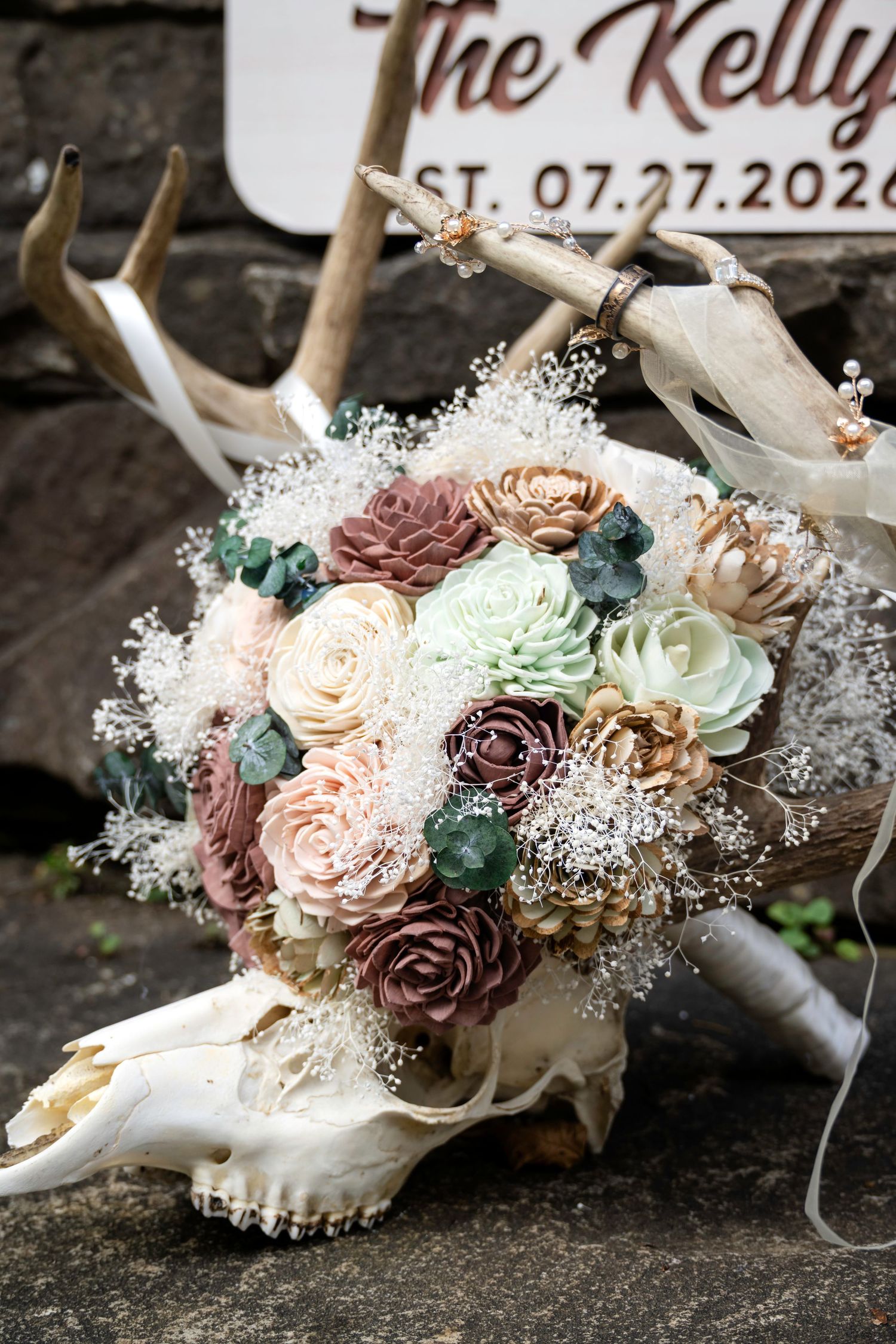 Rustic wedding bouquet with sola wood flowers in mauve and sage resting on deer skull antlers near The Kelly wedding sign.