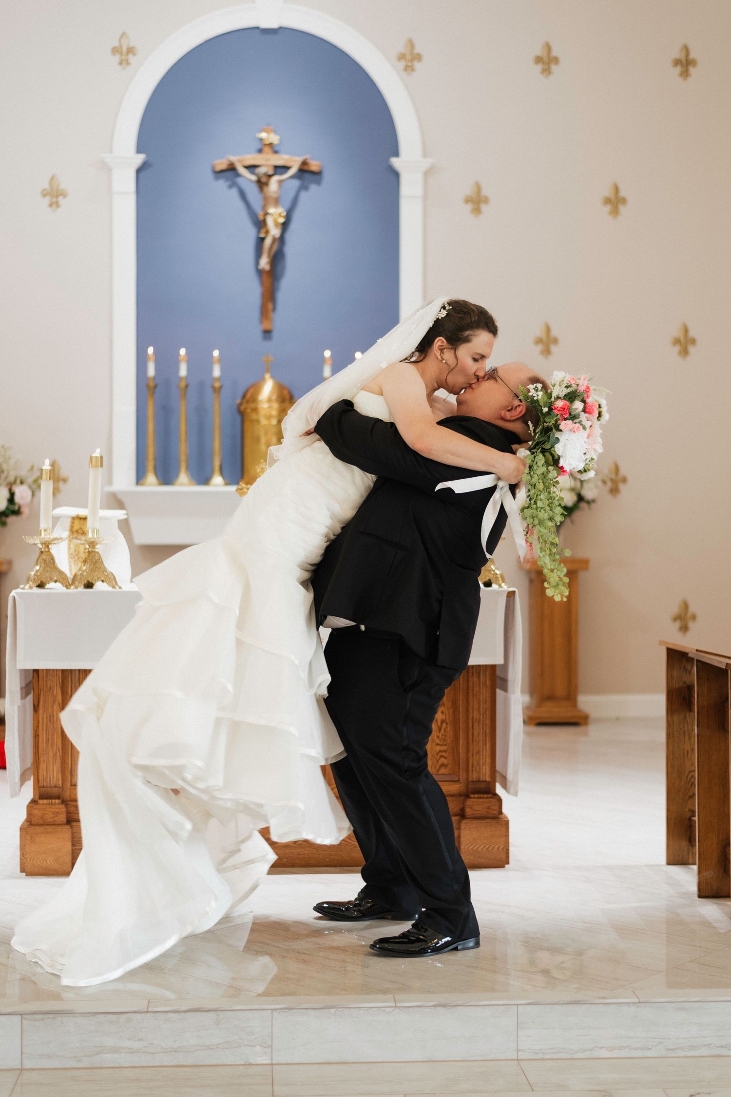 Groom dips bride for romantic kiss at Catholic church altar after wedding ceremony.