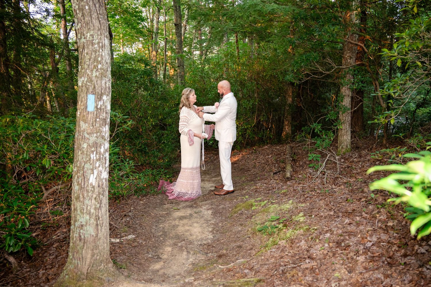 Couple sharing a romantic moment on a forest trail surrounded by lush green trees during an outdoor wedding ceremony.