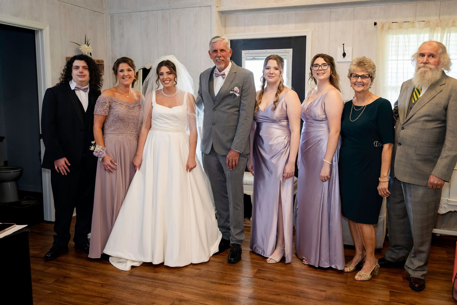 Wedding party group portrait with bride, groom, bridesmaids, and family indoors.