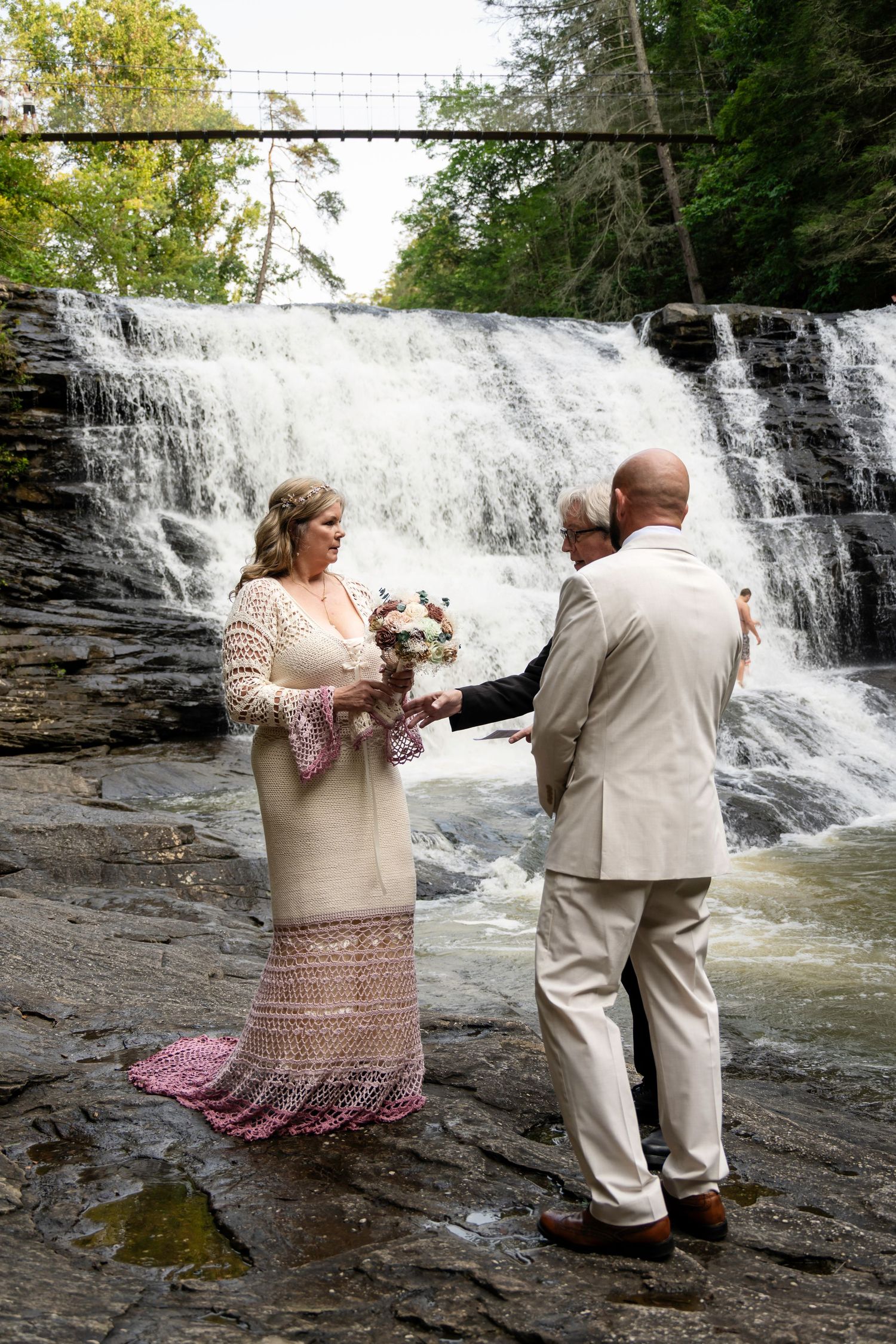 Couple exchanging vows before a stunning waterfall backdrop during an outdoor wedding ceremony on rocky terrain.
