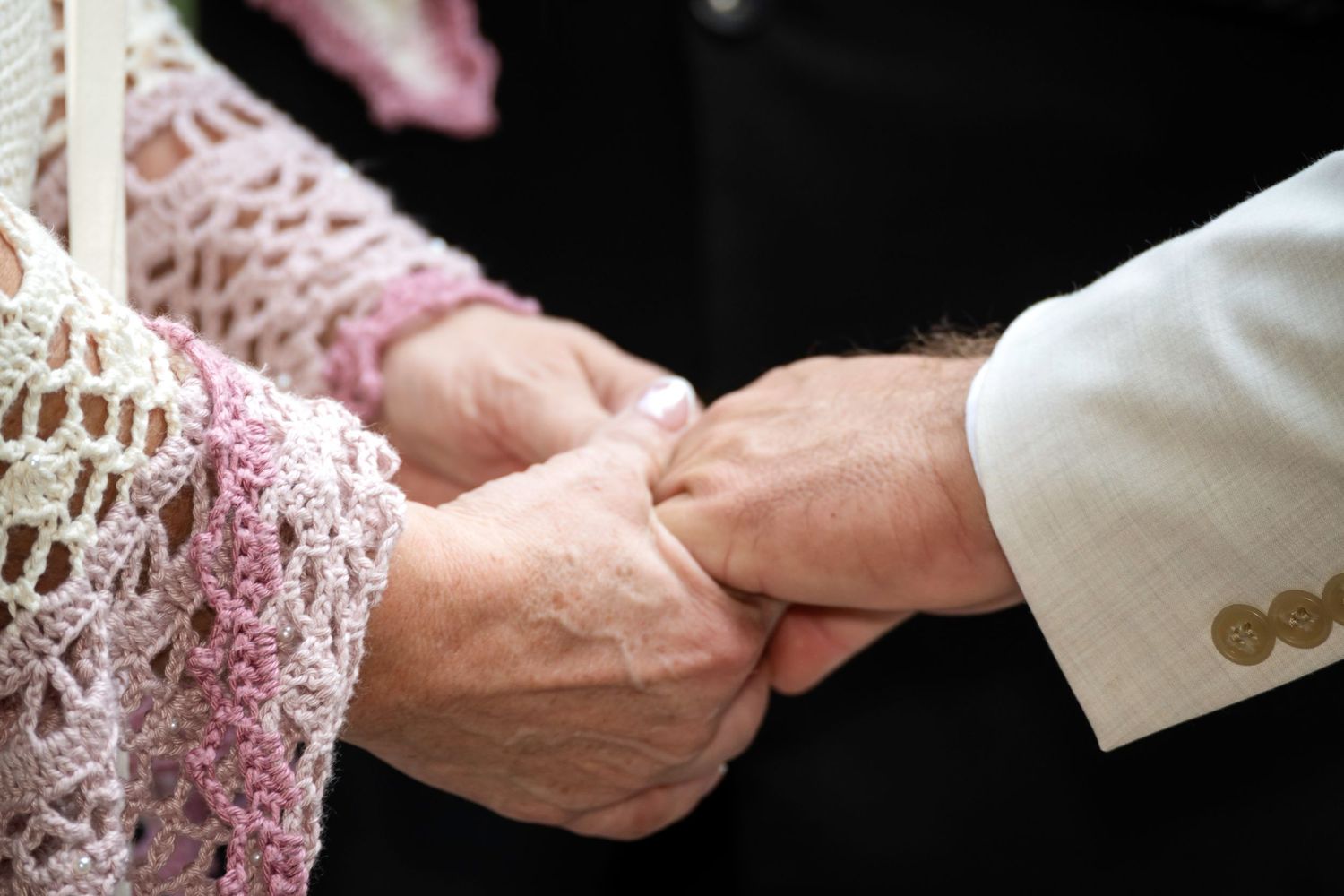 Elderly couple holding hands tenderly, wearing formal attire, symbolizing lasting love and commitment.