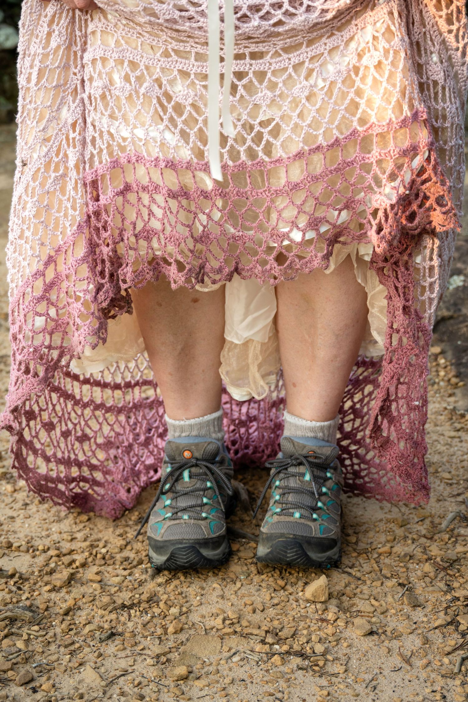 Person wearing a pink crochet lace skirt with hiking shoes and gray socks standing on rocky ground.