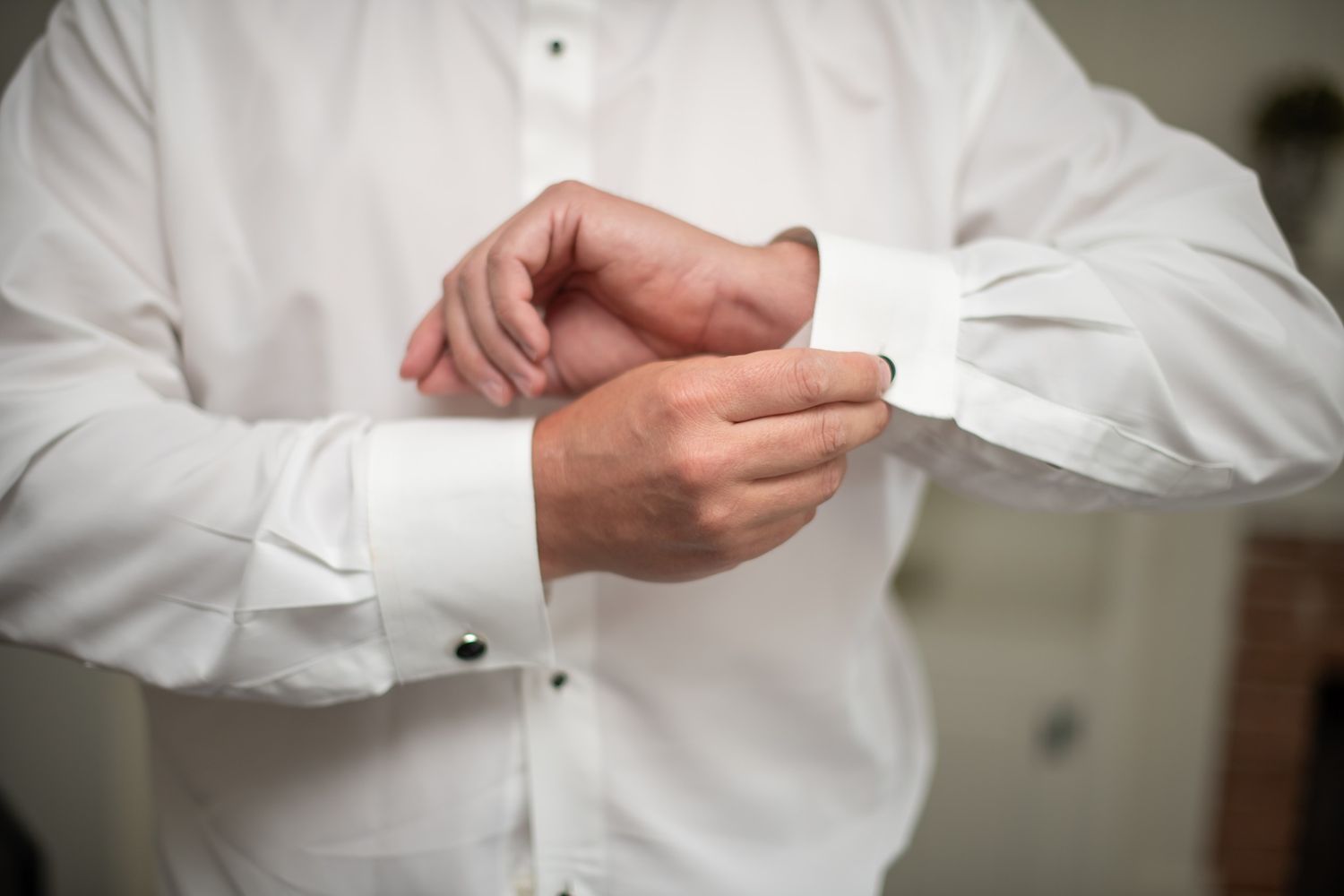 Groom fastening his cufflinks while getting ready in a white dress shirt on wedding day.