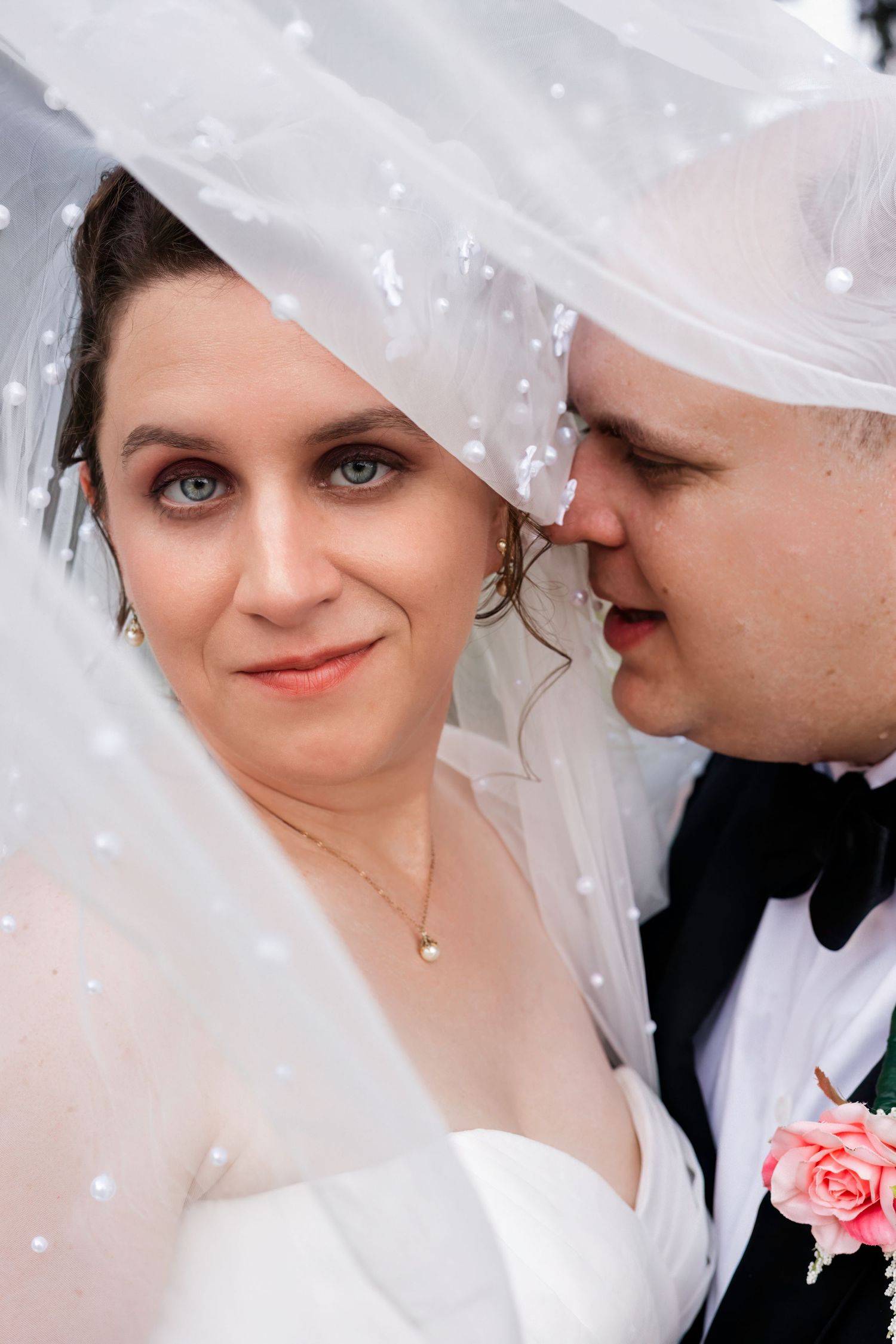 Bride and groom share an intimate moment under a pearl-adorned wedding veil.