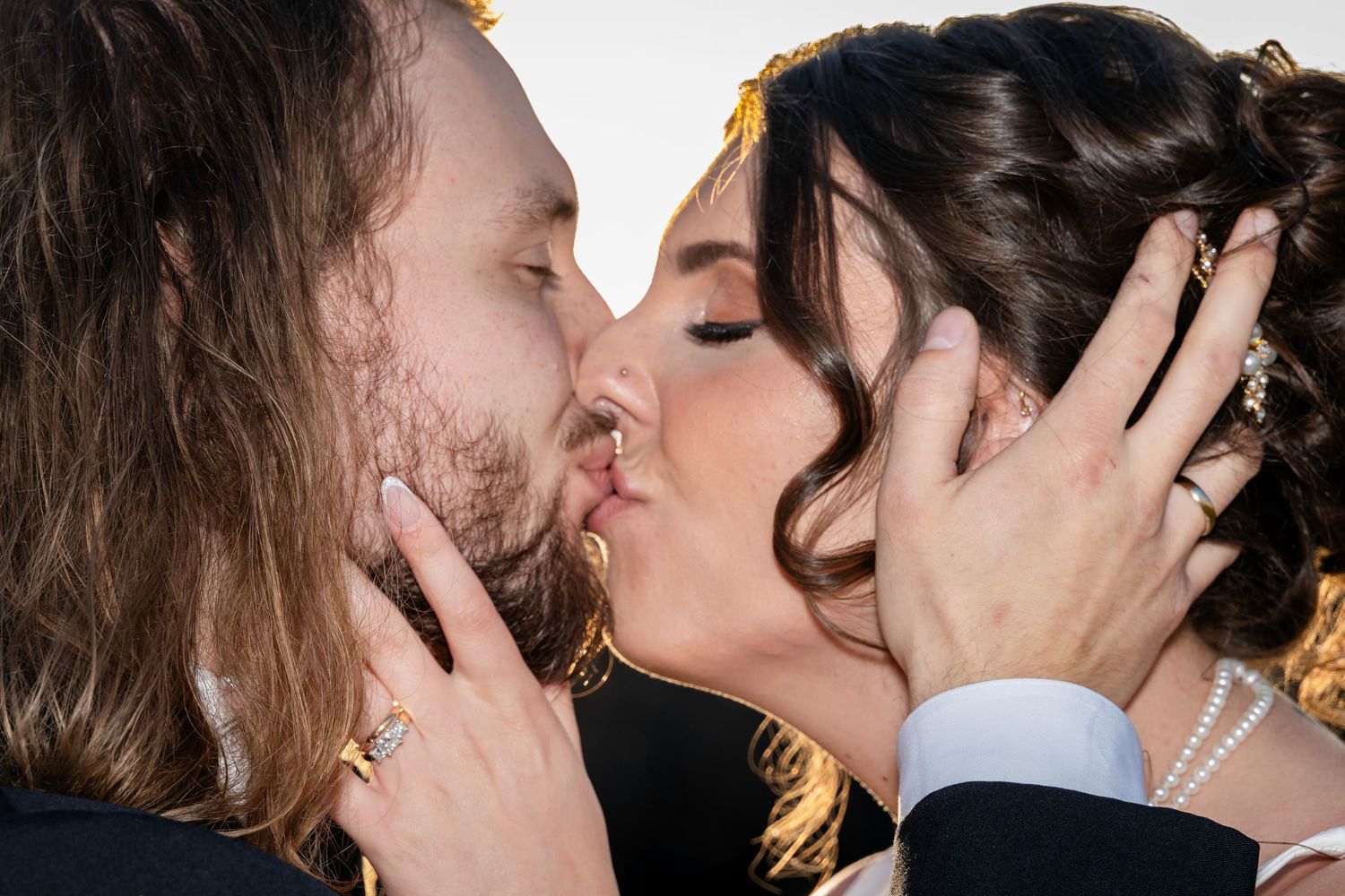 Close-up of bride and groom sharing passionate first kiss with hands on each others faces.