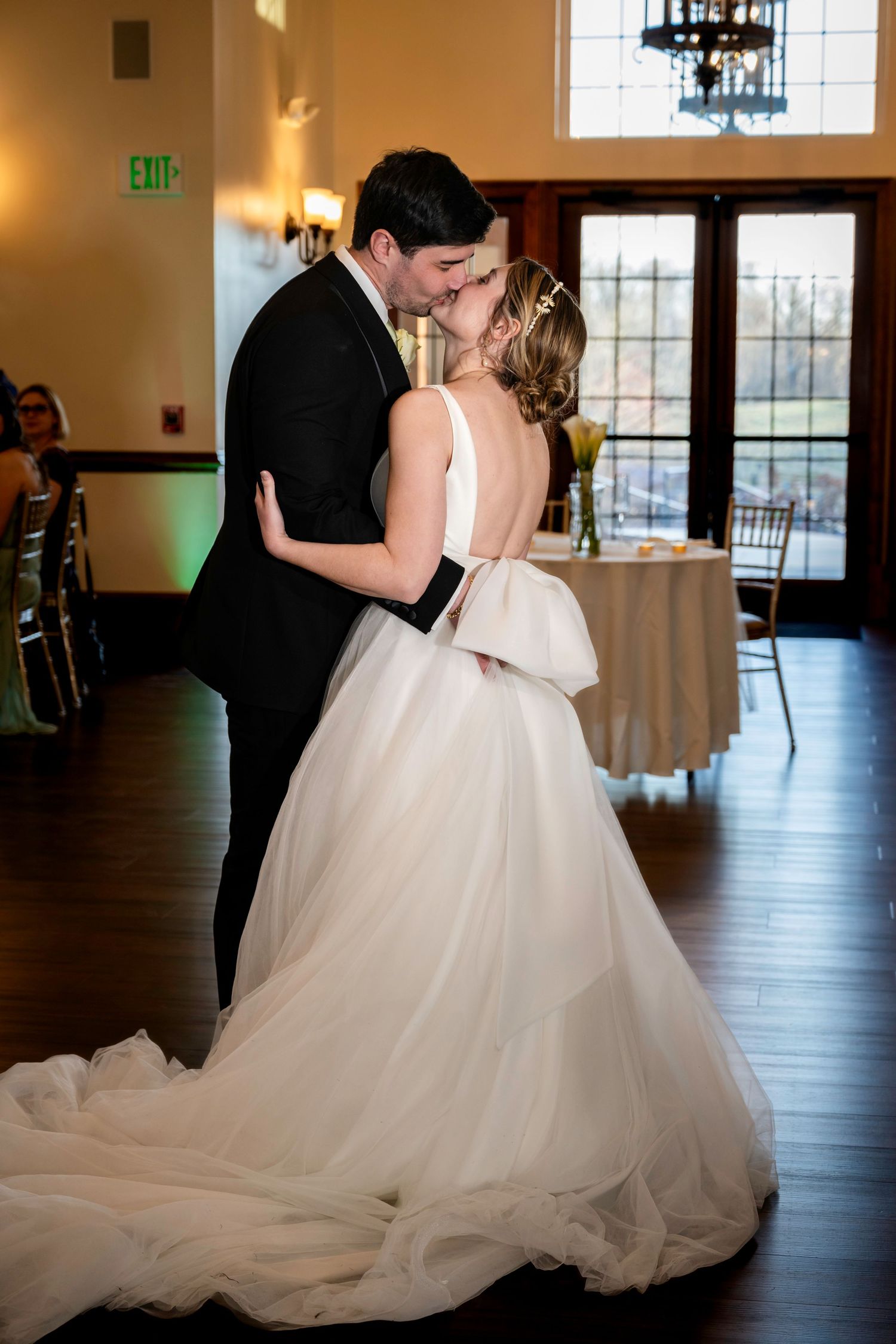 Bride and groom sharing first kiss during wedding reception in elegant venue with warm ambient lighting.