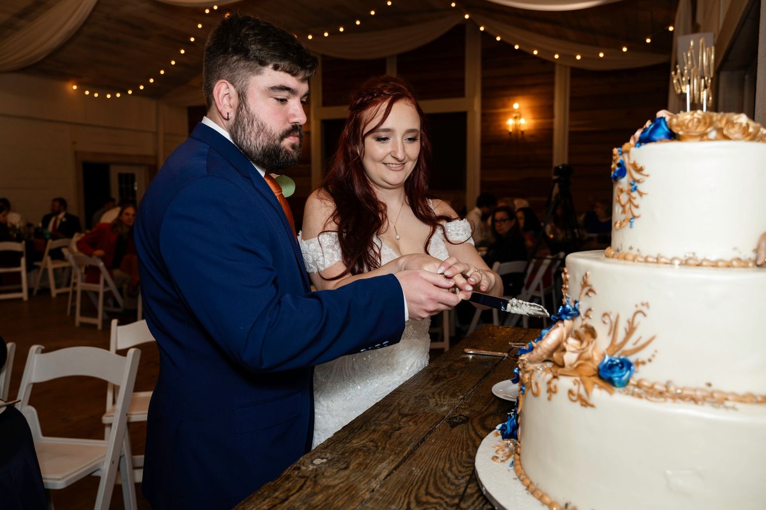 Bride and groom cutting their elegant three-tier wedding cake decorated with gold and blue ocean-themed details.