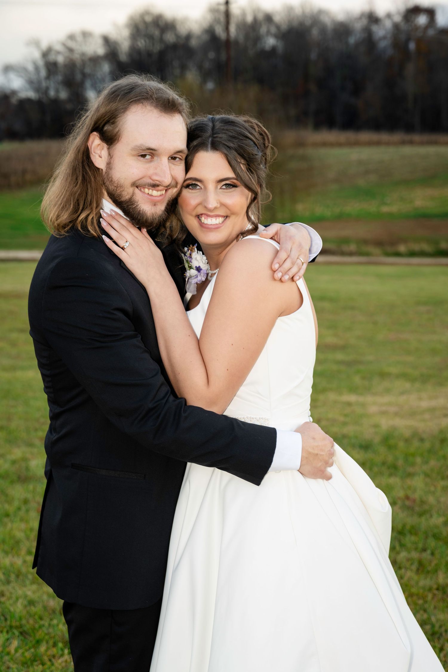 Smiling bride and groom embrace outdoors on green grass at golden hour wedding portrait.