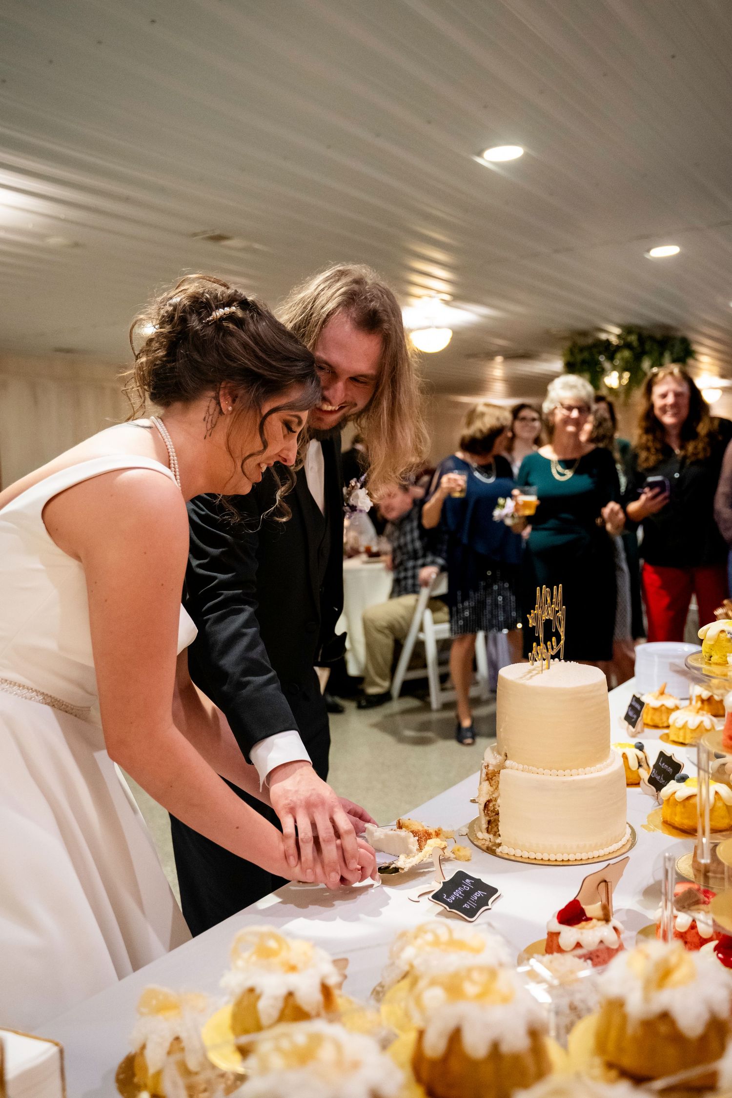 Bride and groom cut wedding cake at reception dessert table.