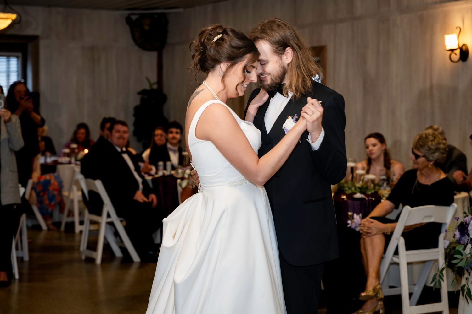 Bride and groom share intimate first dance in elegant reception venue surrounded by seated guests.