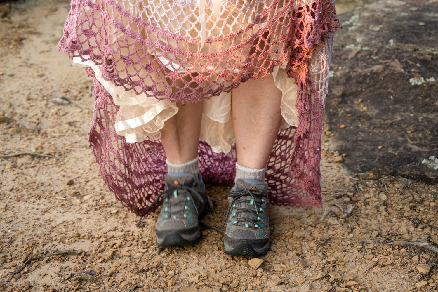 Person wearing hiking shoes and socks under a pink mesh net skirt standing on rocky ground.