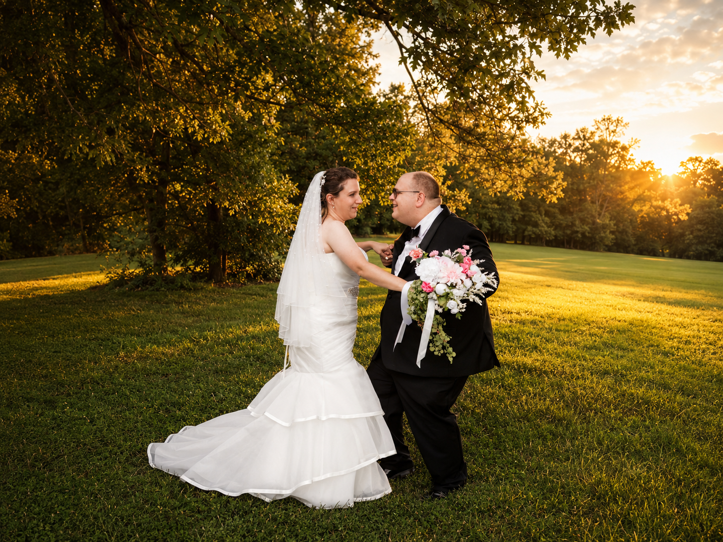 Bride and groom share a romantic dance on lush green grass at golden hour sunset wedding outdoor ceremony.