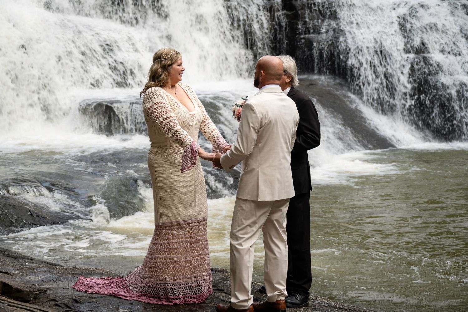 Couple exchanging vows at a waterfall wedding ceremony with an officiant, surrounded by cascading water.