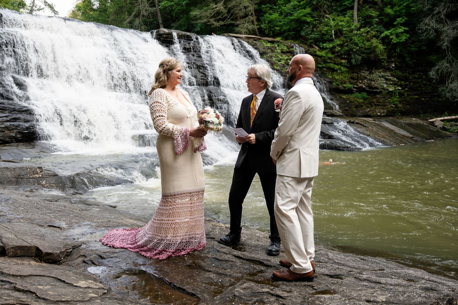 Couple exchanges vows before a stunning waterfall with an officiant during an intimate outdoor elopement ceremony.