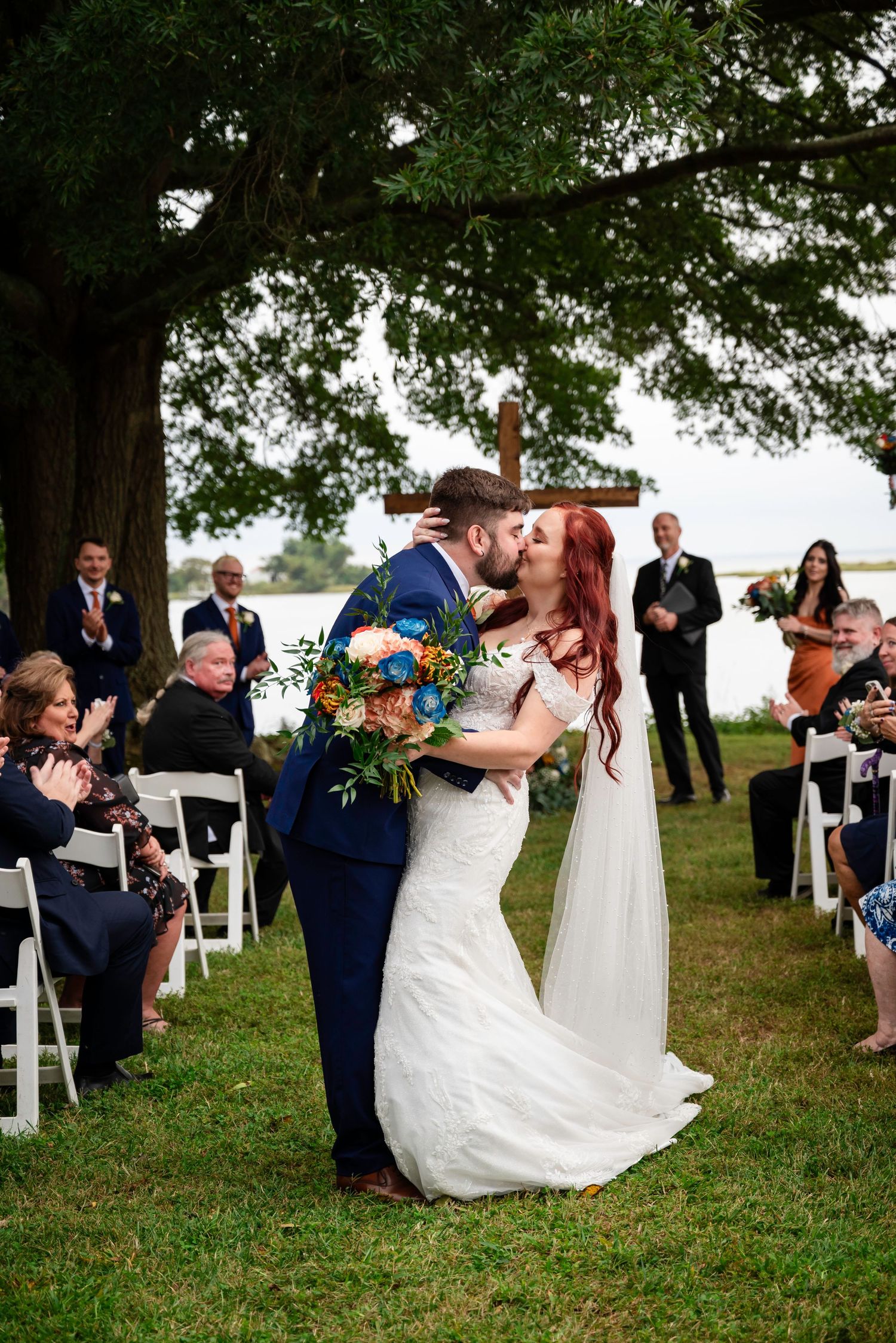 Bride and groom share their first kiss at an outdoor lakeside wedding ceremony.
