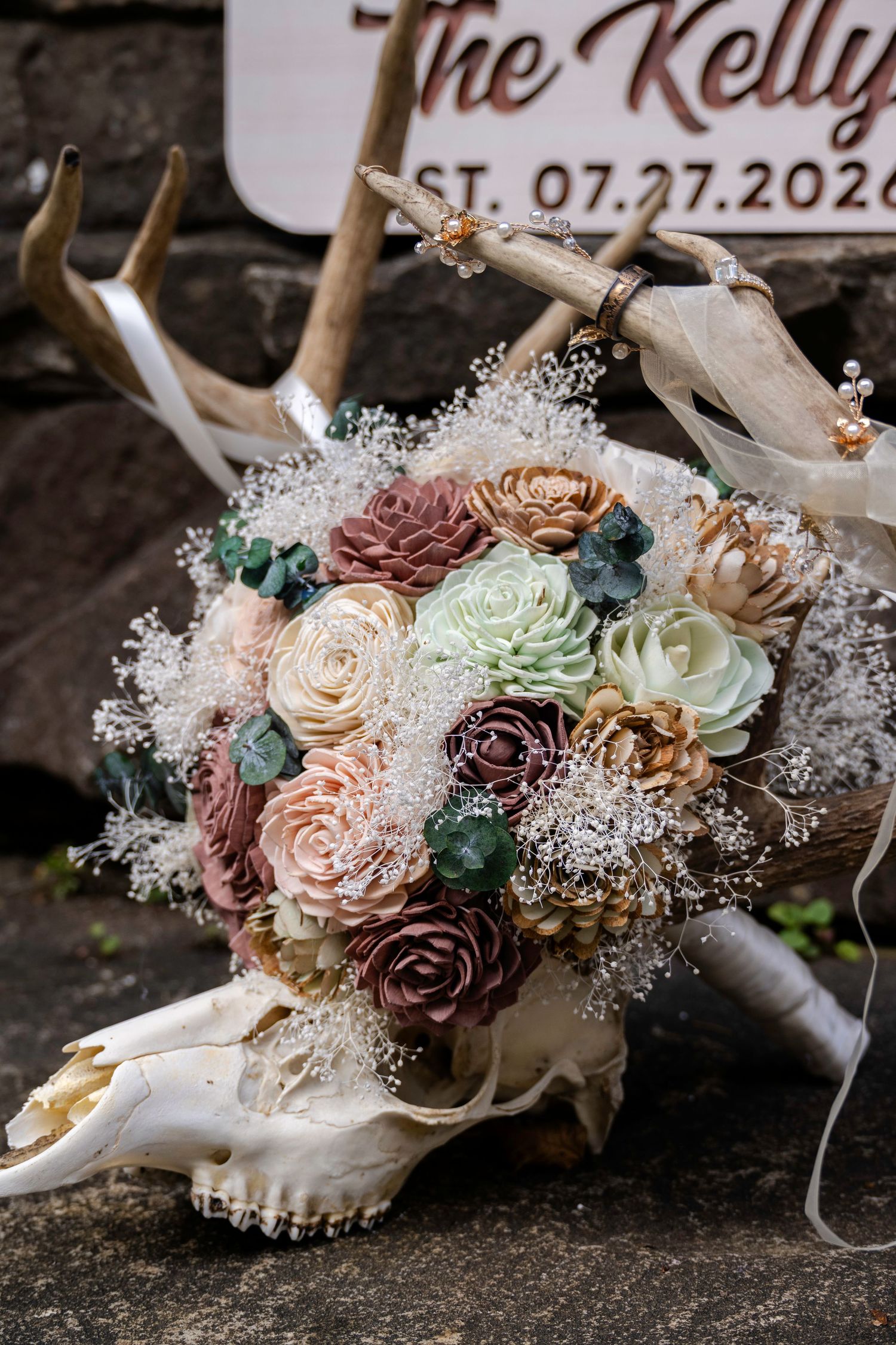 Rustic wedding bouquet with sola wood flowers resting on deer skull antlers, featuring mauve, blush, and sage blooms.