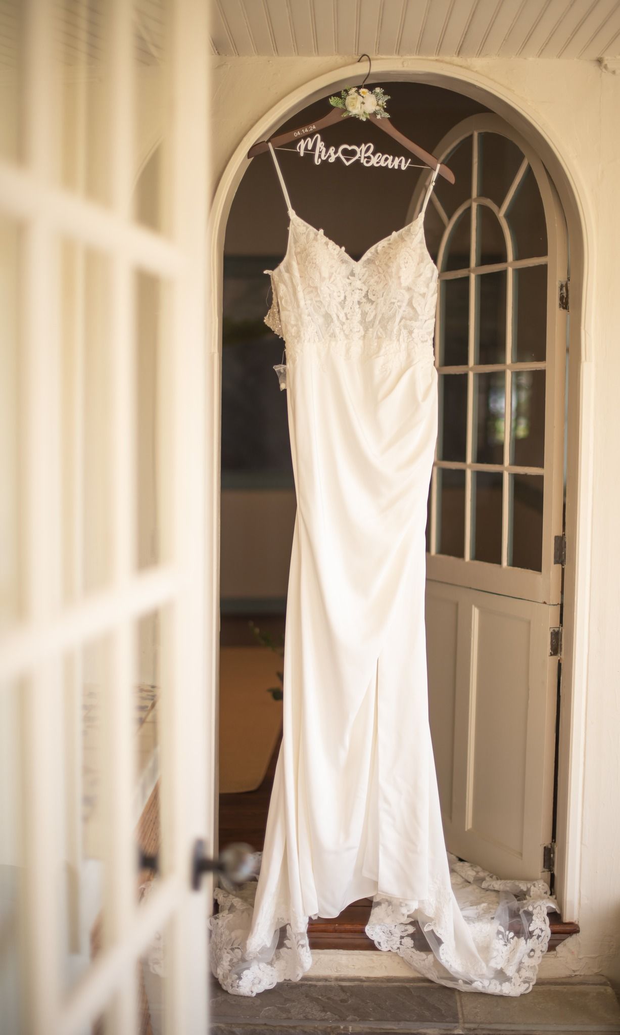 Elegant white wedding dress hanging on a personalized Mrs. Bean hanger in a doorway.