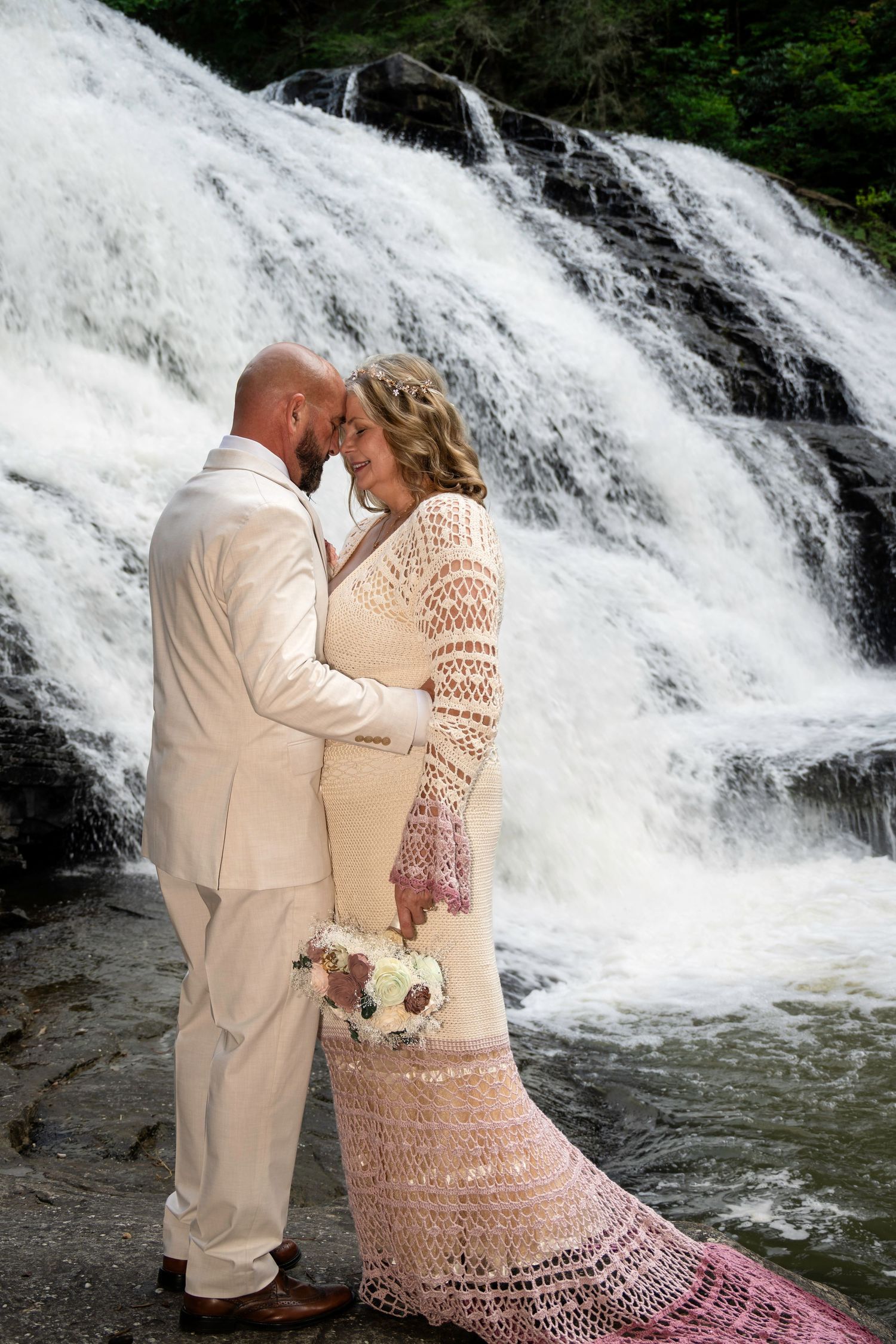 Bride and groom share a romantic moment in front of a stunning waterfall, dressed in elegant white wedding attire.
