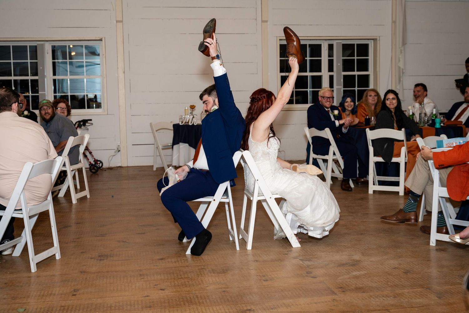 Bride and groom playfully raise their shoes during the wedding shoe game at their reception.