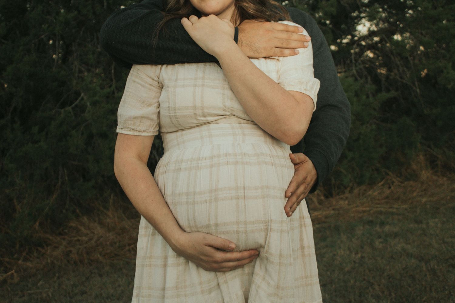 copperas cove maternity photographer capturing husband hugging pregnant mother in nature at golden hour.