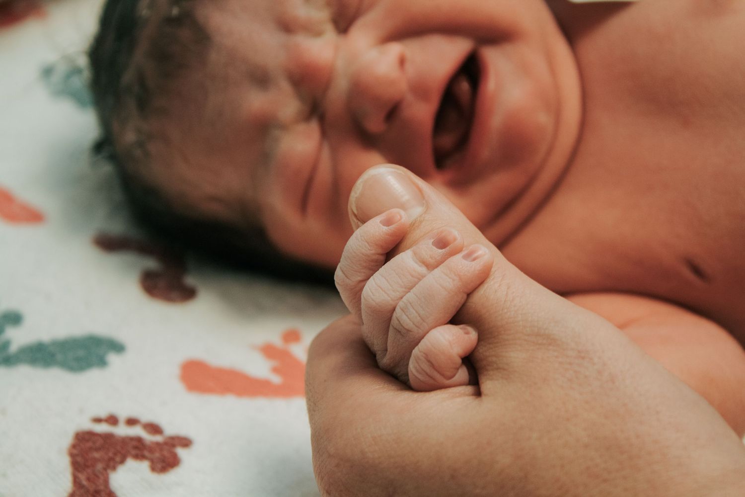 Copperas Cove Birth Photographer captures crying newborn in baby warmer with dad's thumb in her hand.