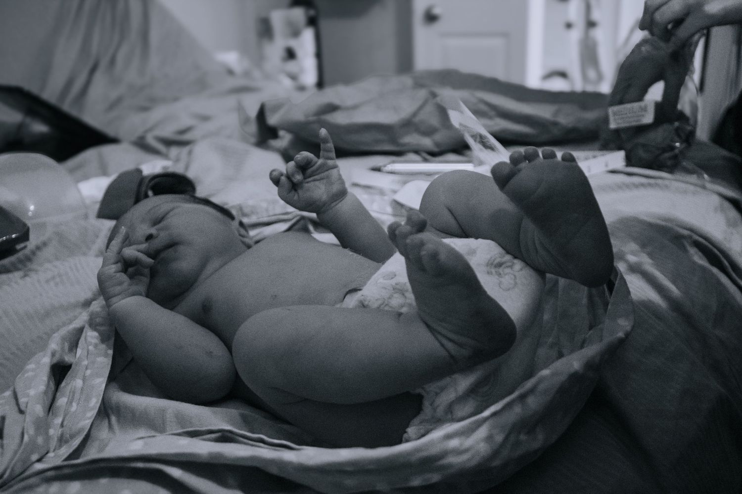 Killeen Birth Photographer captures newborn baby laying on bed after being weighed in a scale sling.