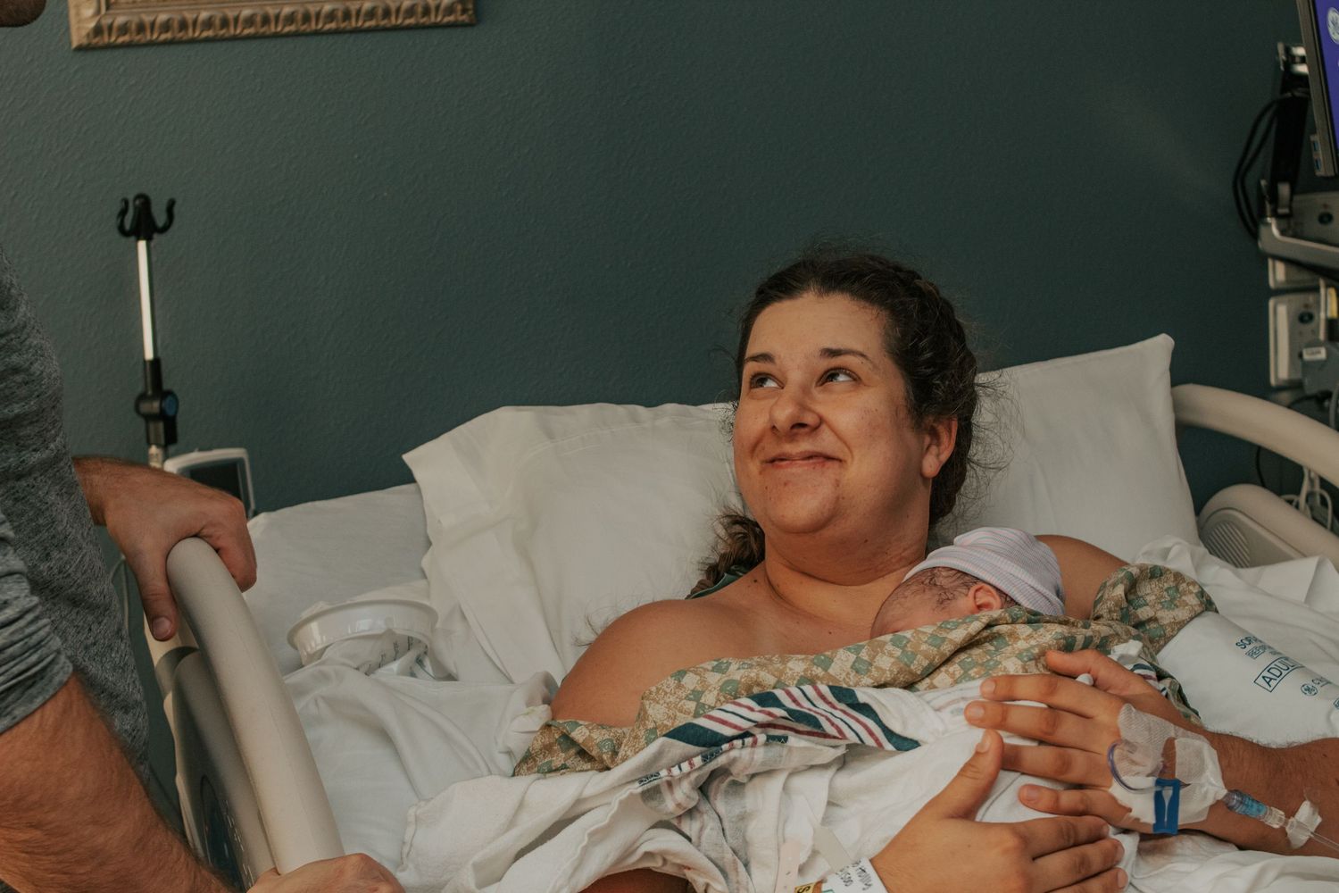 Copperas Cove birth photographer capturing New mother smiling in hospital bed after giving birth, holding newborn baby.