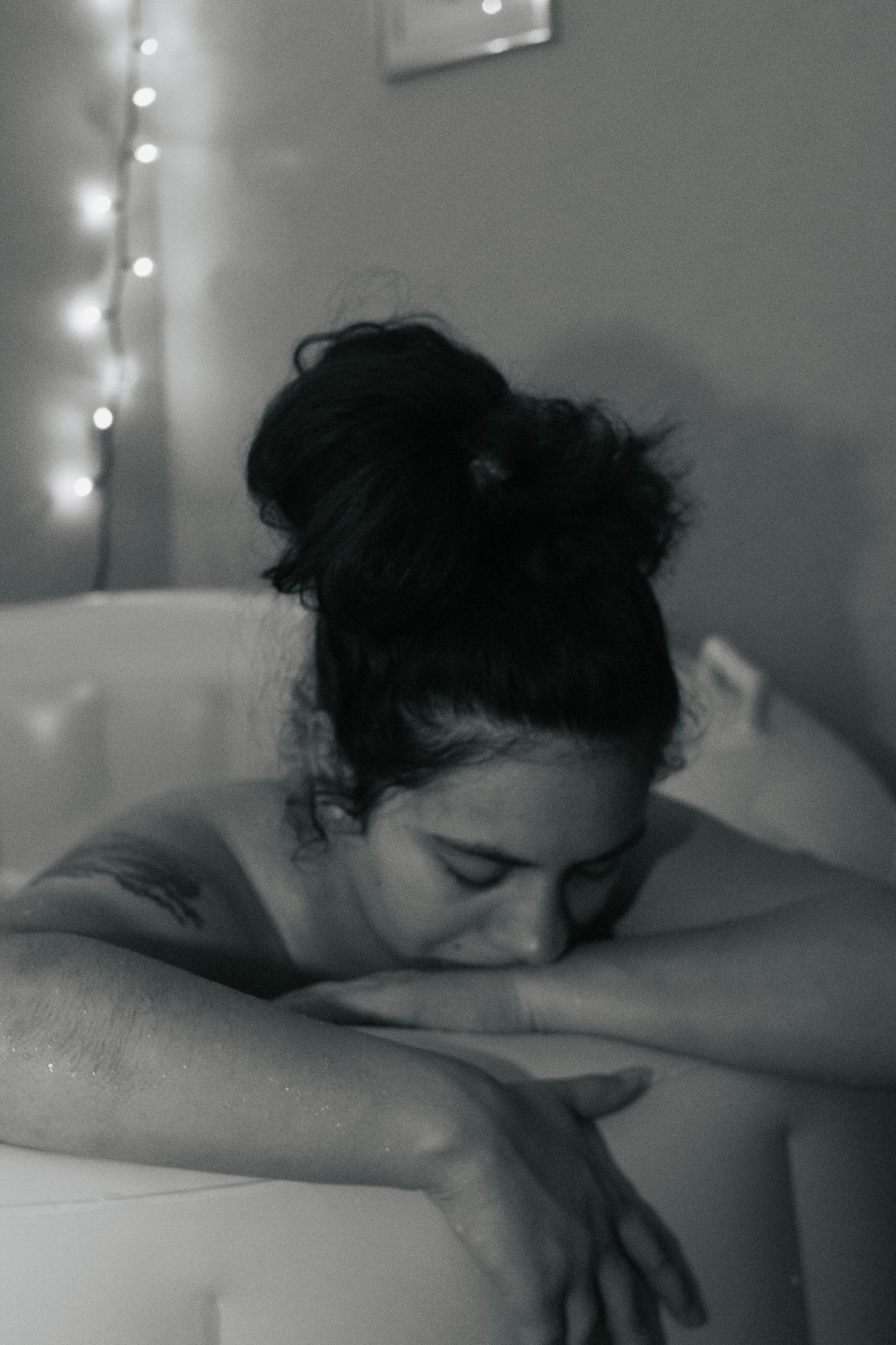 Fort Hood Birth Photographer captures laboring mother leaning on the side of the birth pool with twinkle lights in the background.