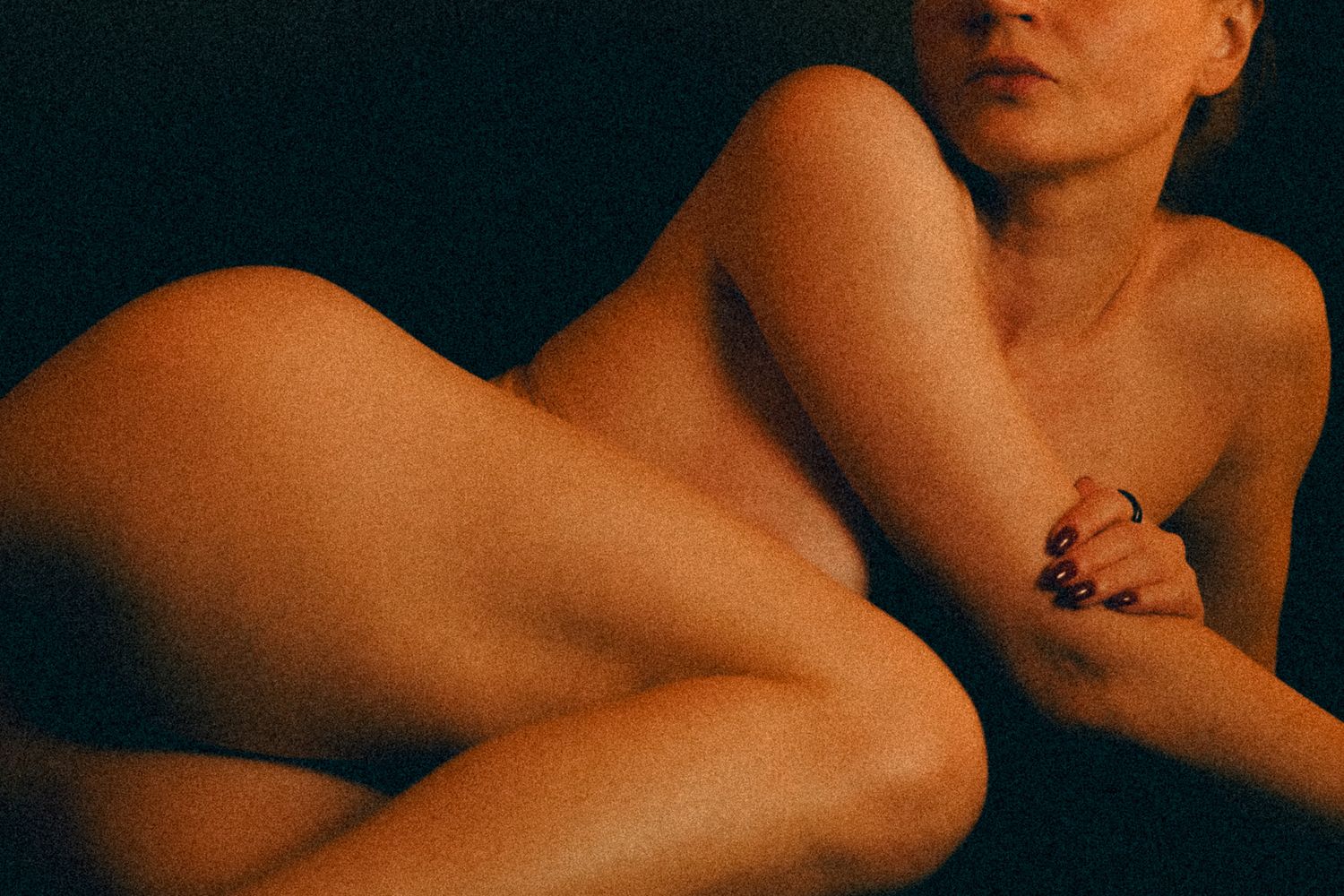 Abstract artistic nude study in warm tones showing curved forms against dark background.