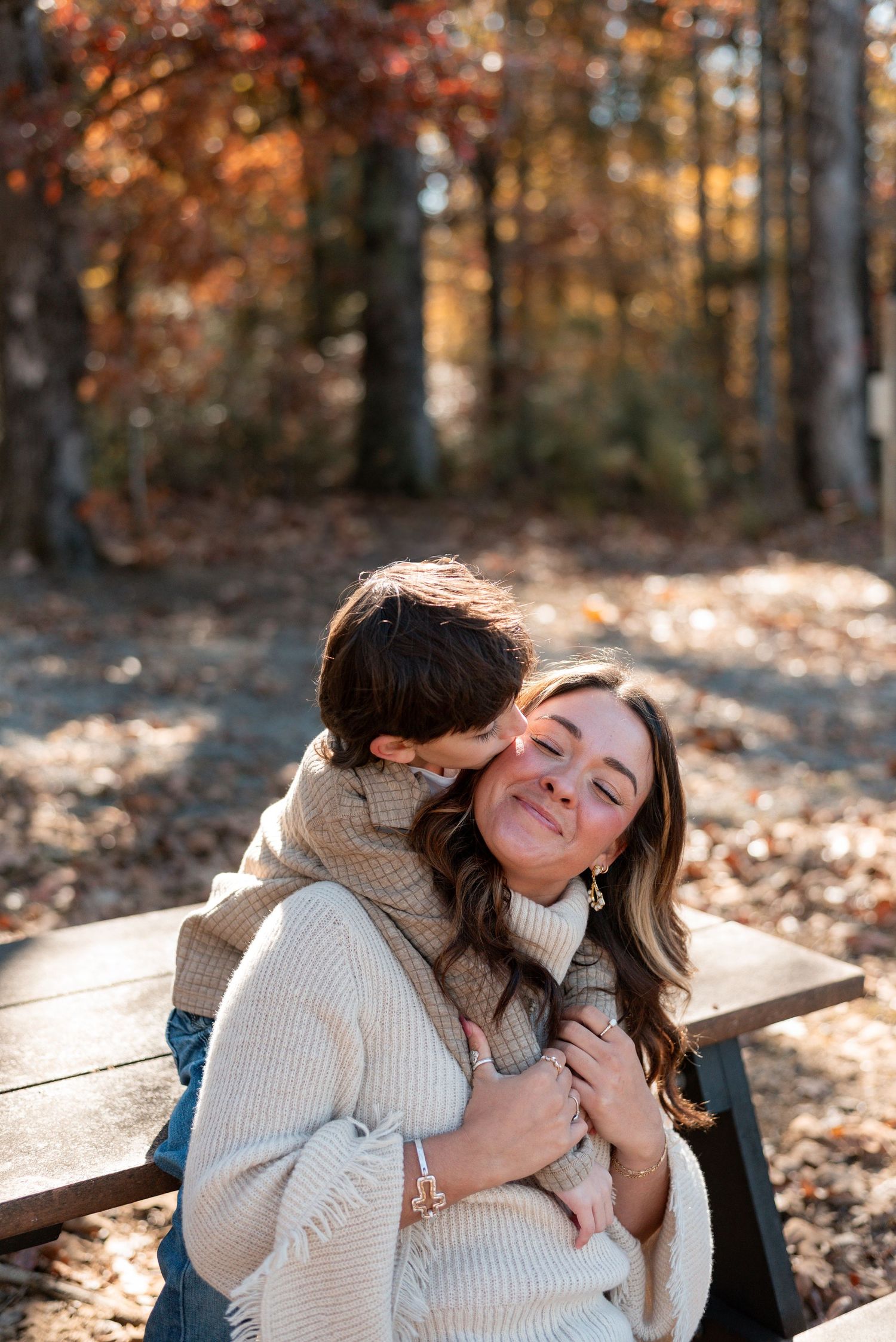 A couple shares a tender moment while laying in autumn leaves during a golden hour photoshoot.