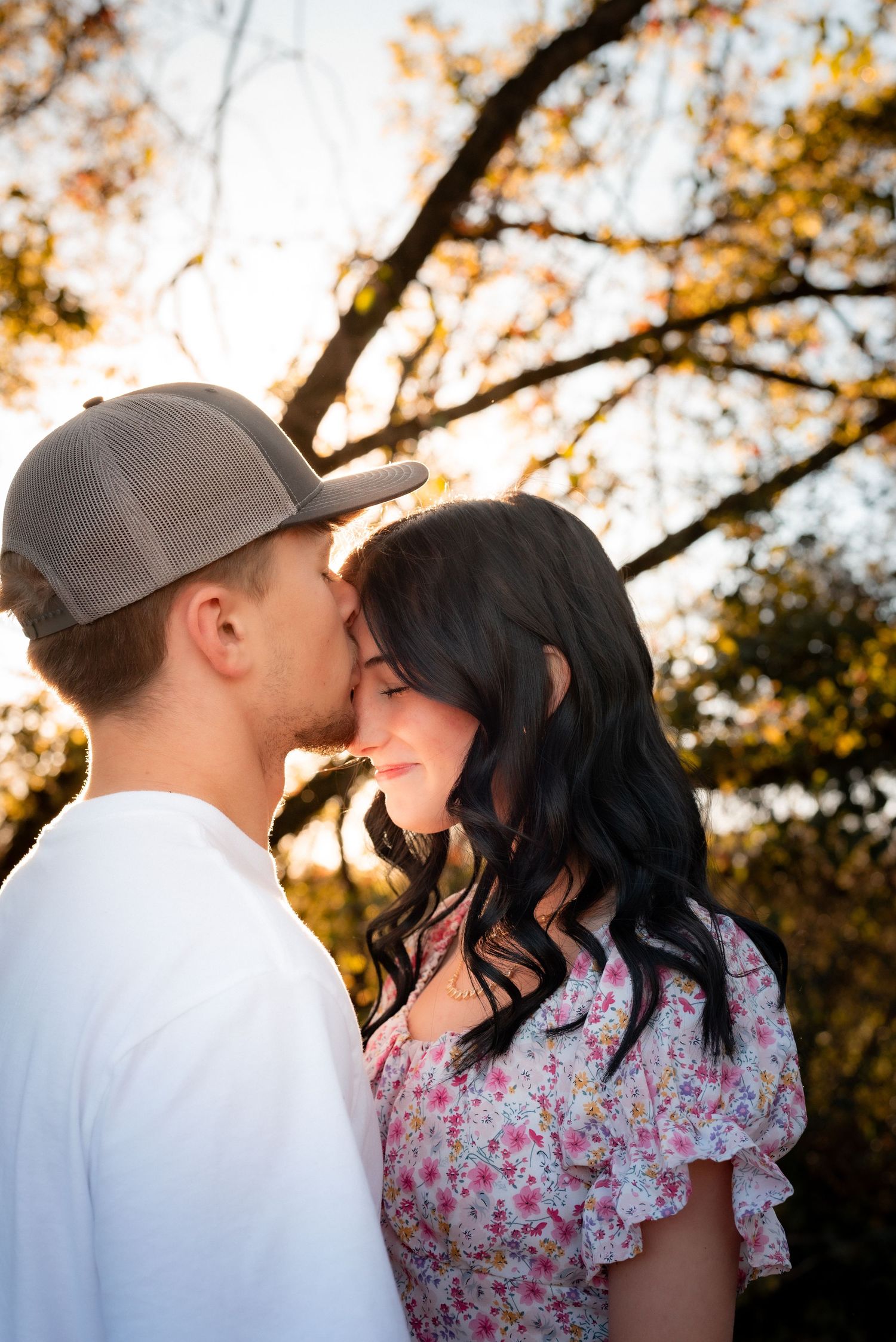 A tender moment captured between two people against a backdrop of autumn trees at sunset.