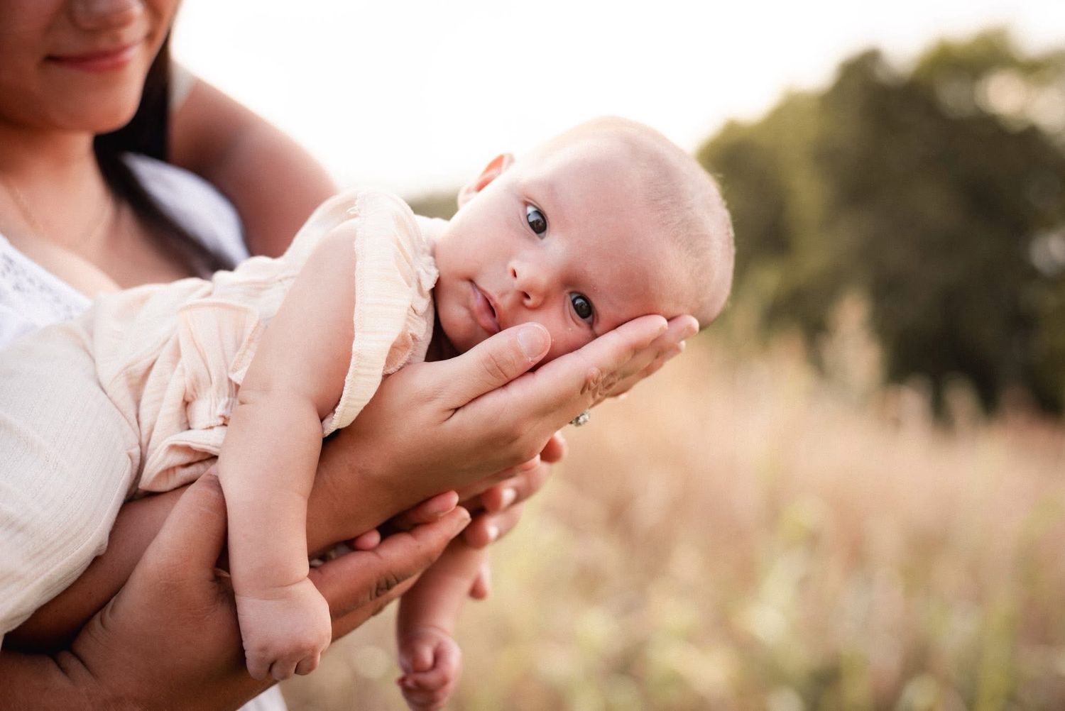Gentle hands holding baby against soft natural background.